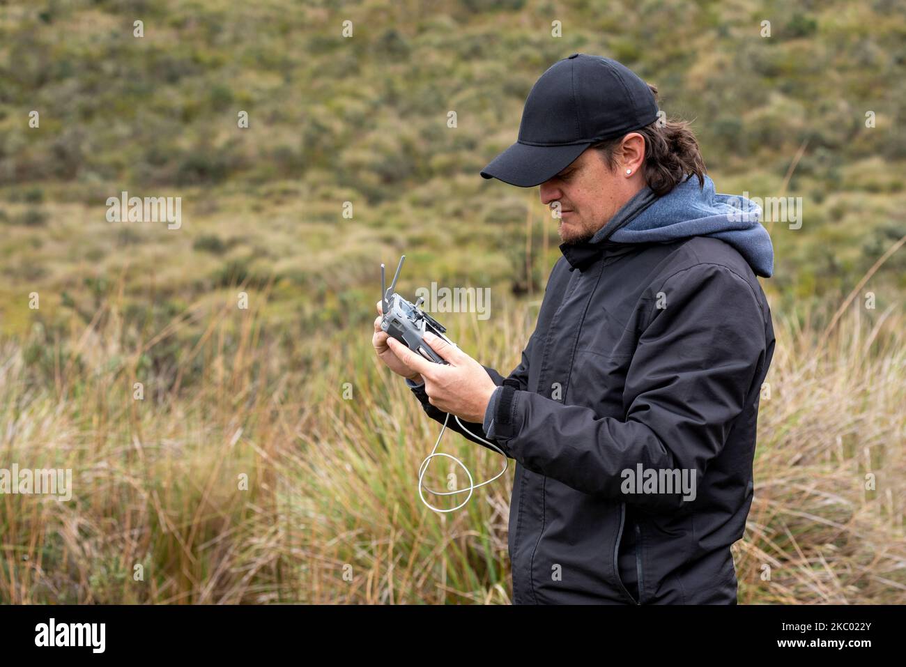 Ein junger hispanischer Mann in einer Kappe, der tagsüber eine Drohne auf einem Feld betreibt Stockfoto