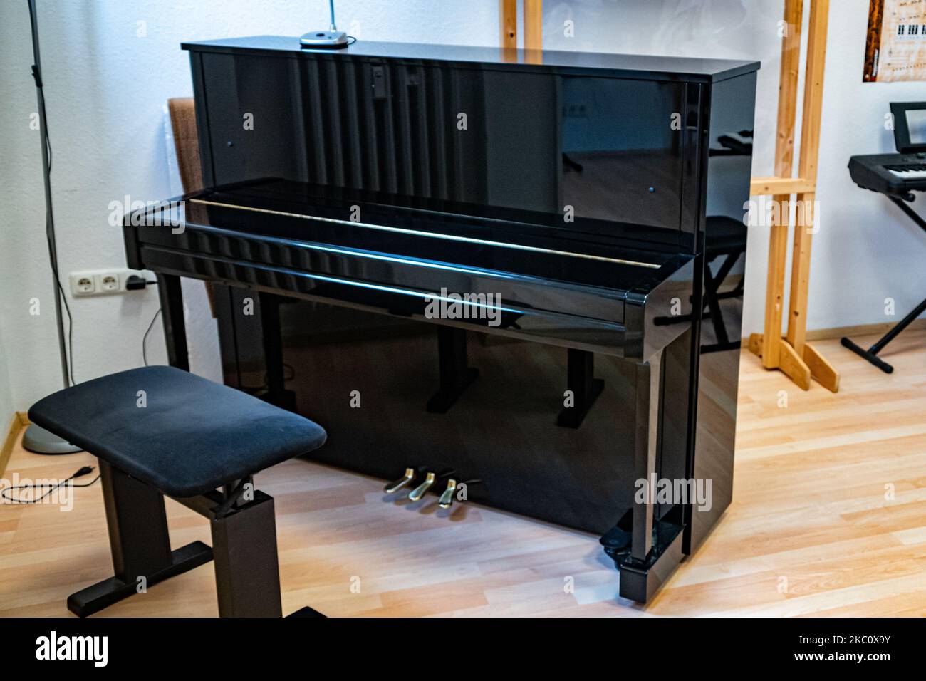 Ein altes schwarzes Klavier mit einem Hocker davor Stockfoto