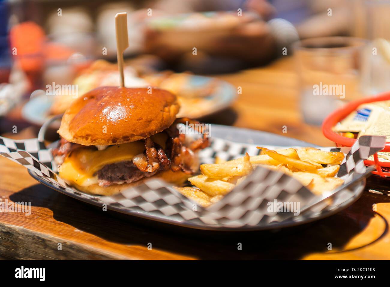 Ein weicher Fokus aus einem appetitlichen Burger mit Käse und Speck, serviert mit Pommes auf der Seite Stockfoto