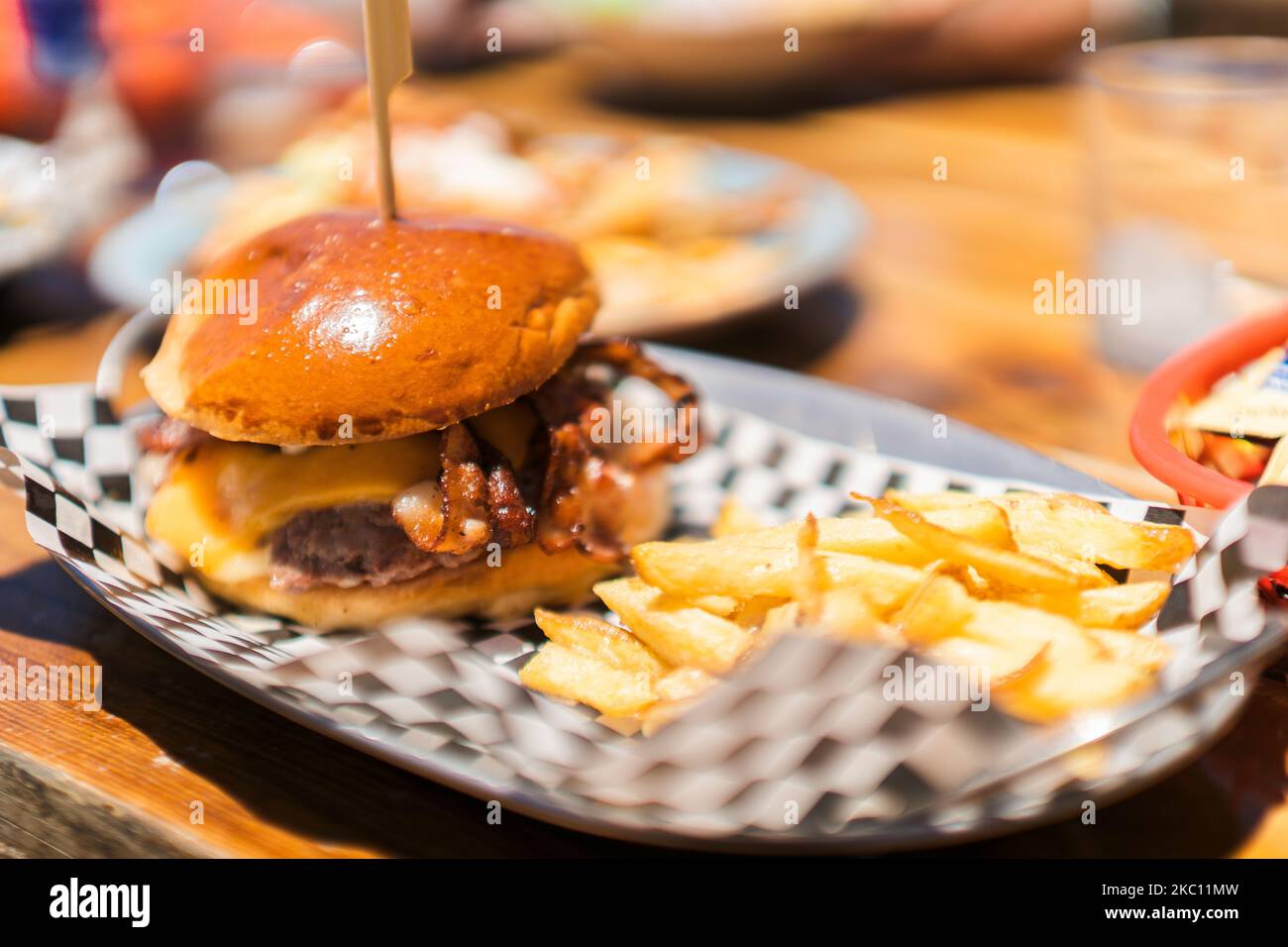 Ein weicher Fokus aus einem appetitlichen Burger mit Käse und Speck, serviert mit Pommes auf der Seite Stockfoto