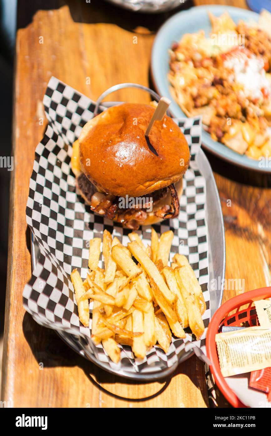 Ein vertikaler Schuss eines appetitlichen Burger mit Käse und Speck serviert mit Pommes auf der Seite Stockfoto