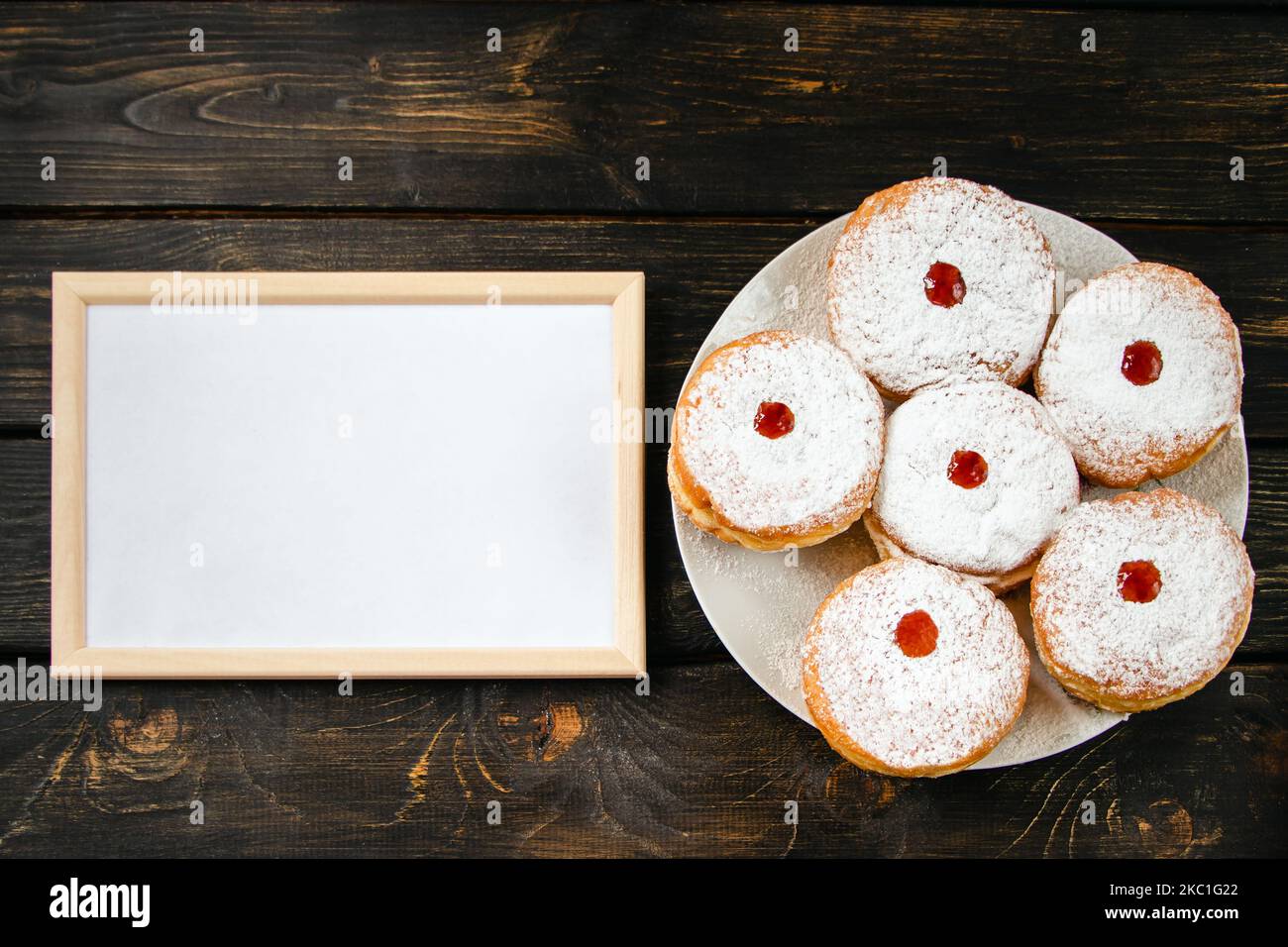 Frohes Chanukka. Leerer Rahmen für Glückwunschtext und traditionelles Dessert Sufganiyot auf dunklem Holzhintergrund. Jüdische religiöse Holida feiern Stockfoto