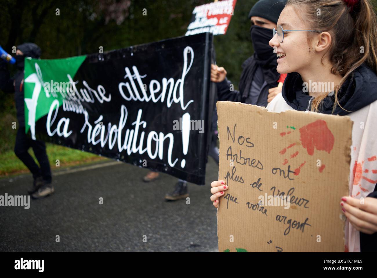 Eine junge Frau hält einen Karton mit der Aufschrift „Unsere Bäume sind wertvoller als Ihr Geld“ in der Nähe eines Spruchbanners „Natue wartet auf die Revolution“. Mehrere Verbände, politische Parteien und Menschen riefen zu einem marsch von Capvern nach Lannemezan in den Pyrenäen auf, als ein globales Unternehmen, Florian, ein riesiges Sägewerk in der Nähe der Pyrenäenstadt Lannemezan bauen will. Das Sägewerk wird voraussichtlich fast 400,000 Kubikmeter Buchenholz pro Jahr behandeln. Dafür muss Florian in allen französischen Pyrenäen Buchen schneiden. Sie beabsichtigt, beschneidete Wälder zu räumen. Die Demonstranten kamen aus fast allen französischen PY Stockfoto