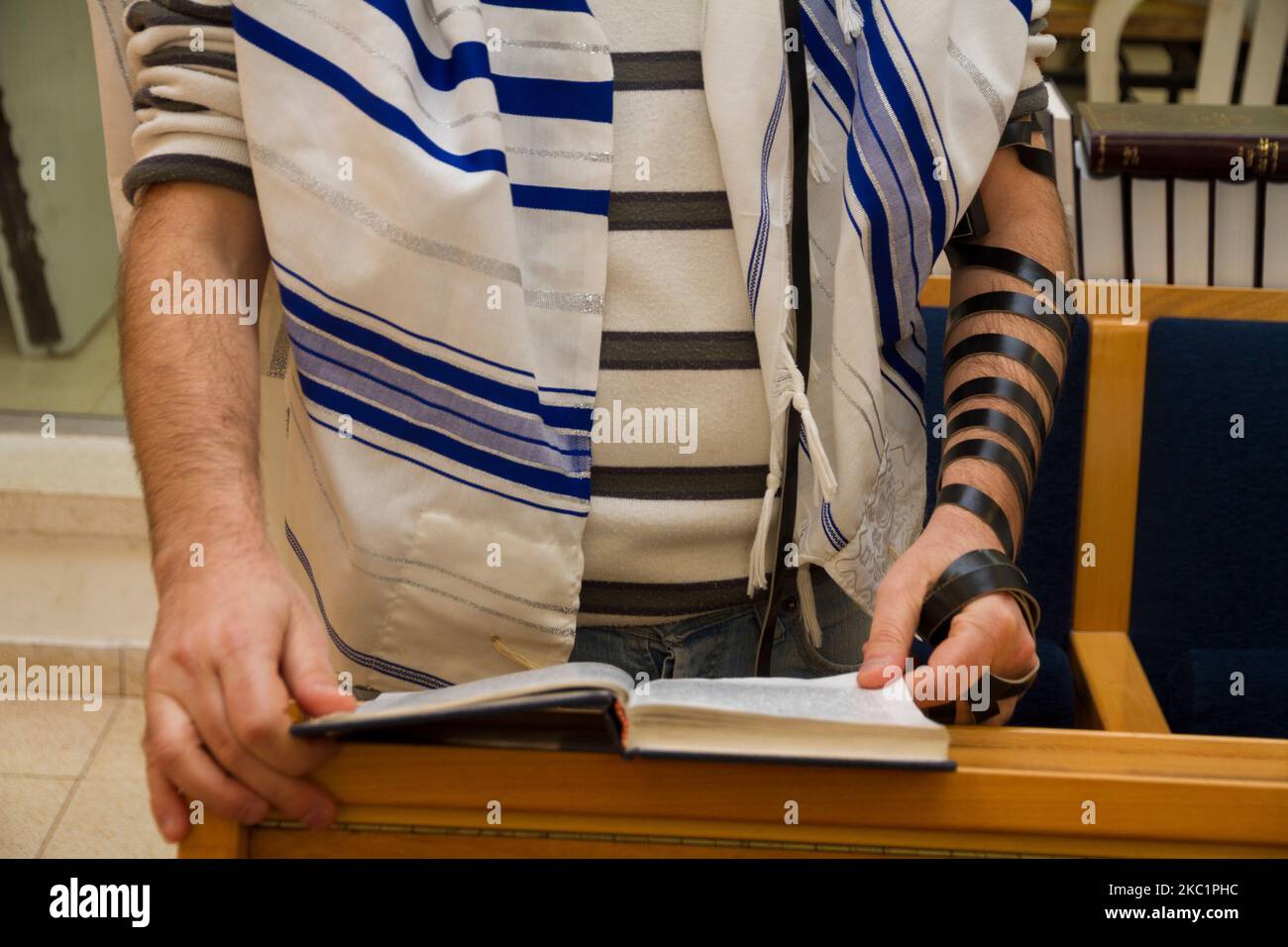 Ein erwachsener jüdischer Mann, der mit einem Tefillin auf seinem Arm betet, ein bibelbuch hält, während er ein Gebet bei einem jüdischen Ritual liest Stockfoto