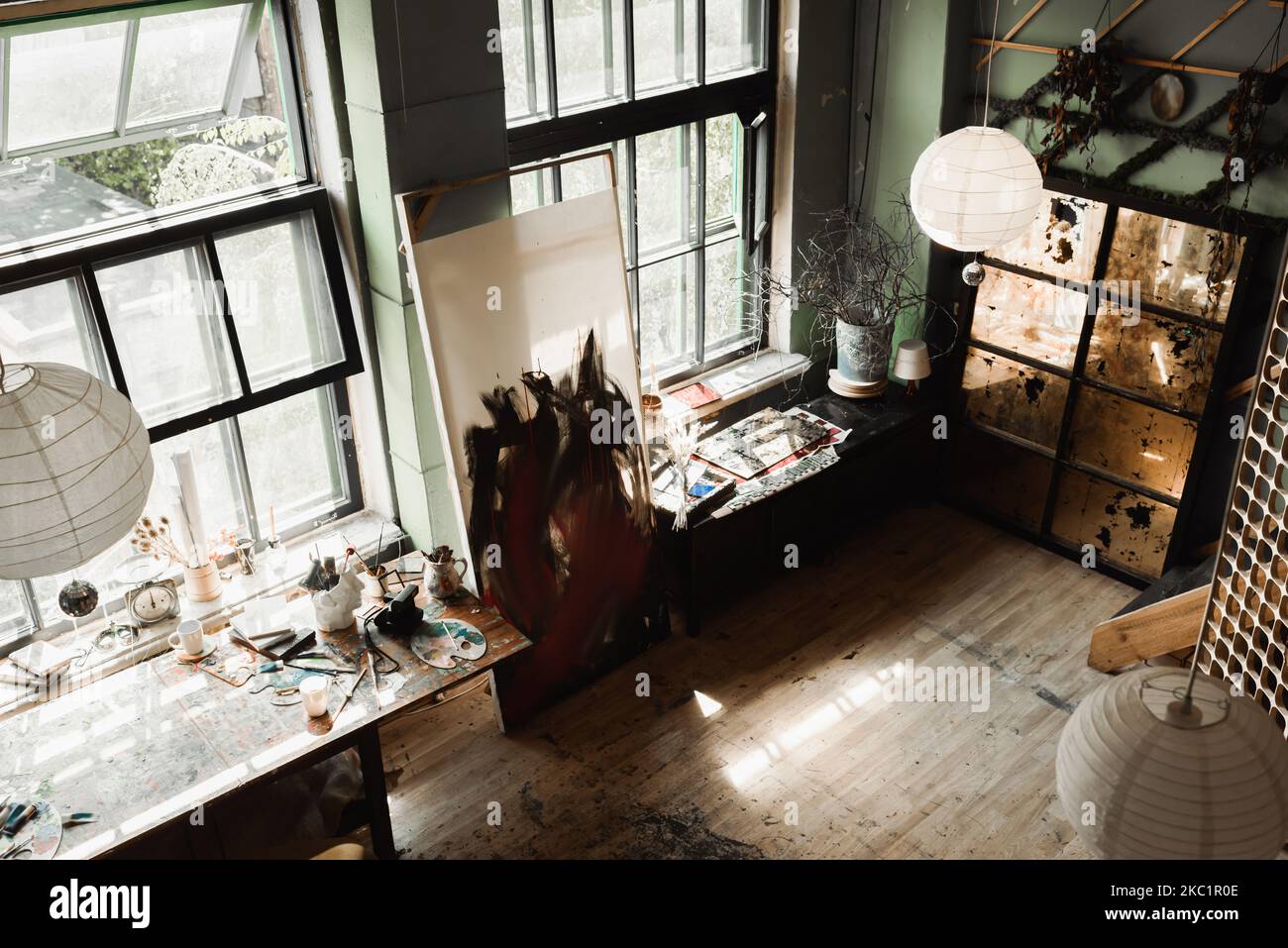 Blick auf die geräumige Werkstatt mit großen Fenstern und Kunstwerkzeugen auf Fensterbänken unter Kugelkronleuchtern Stockfoto