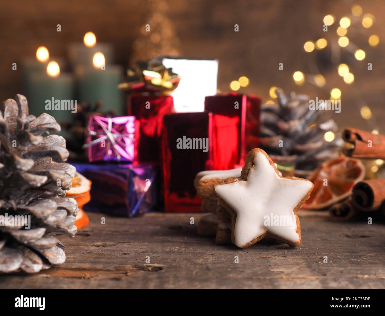 Gestapelte Zimtsterne auf einem Holztisch mit bunten Geschenkschachteln und verschwommenen Weihnachtslichtern Stockfoto