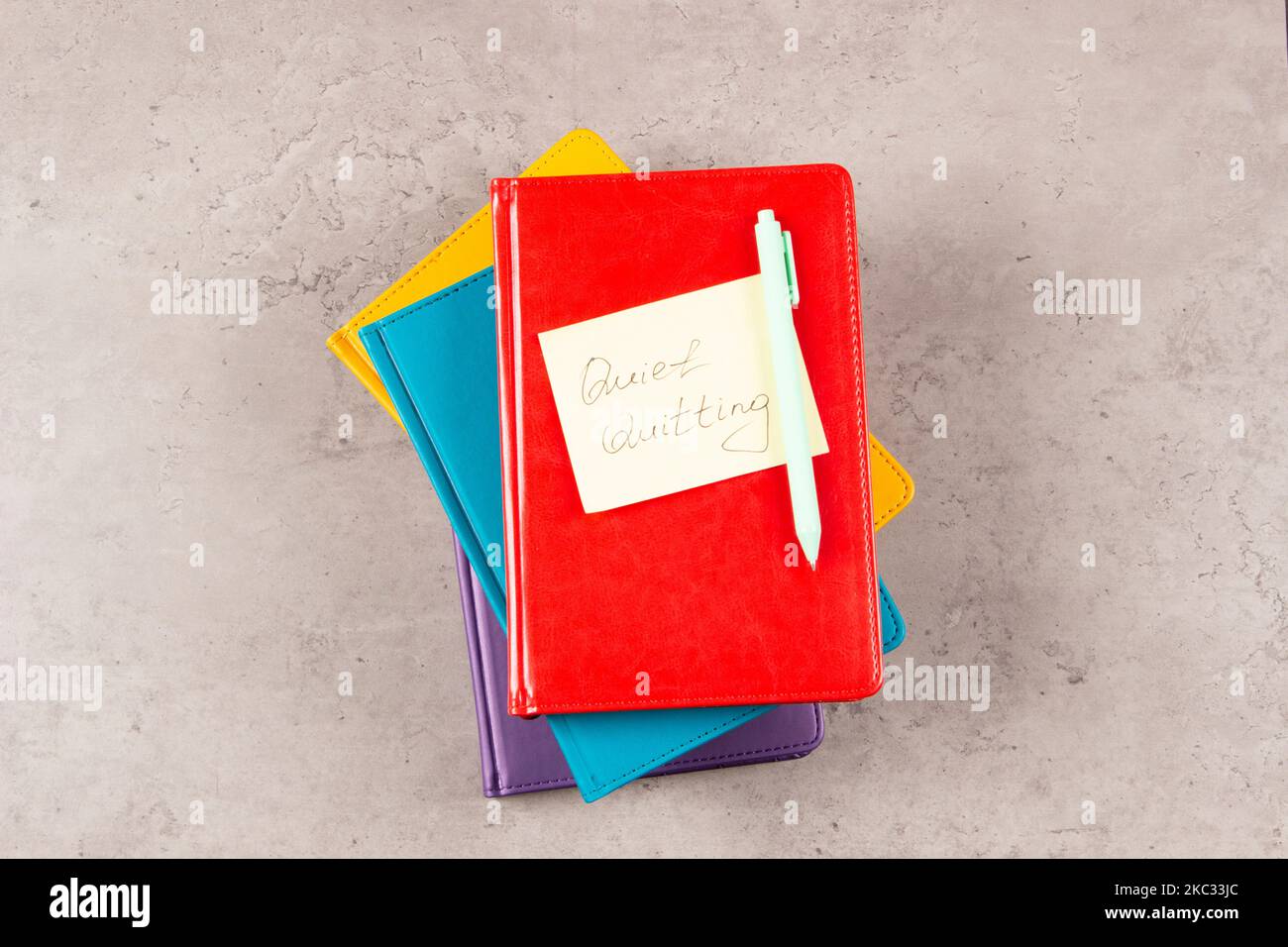 Papierstapel Business Notebook-Planer und Haftnotiz mit Text Quiet Quitting auf dem Schreibtisch. Draufsicht. Work-to-Rule, bei dem Mitarbeiter arbeiten Stockfoto