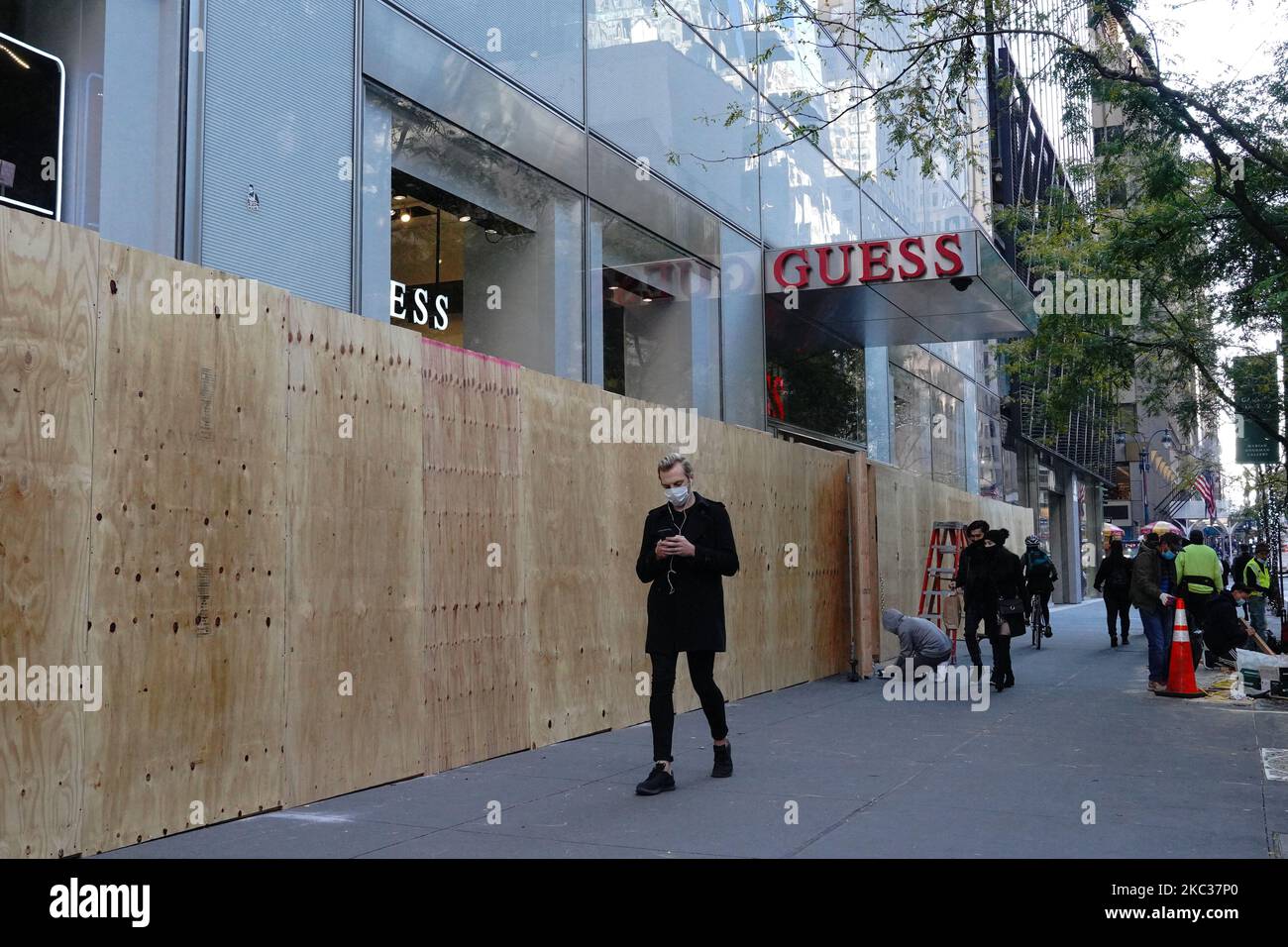 Maskierte Menschen kommen an einem Guess-Store vorbei, während Arbeiter in Erwartung der Unruhen im Zusammenhang mit den Präsidentschaftswahlen am 2. November 2020 in New York City an Bord gehen. Grundstückseigentümer bereiten sich darauf vor, dass lokale und staatliche Beamte am Wahltag vor Gewalt im ganzen Land warnen. (Foto von John Nacion/NurPhoto) Stockfoto