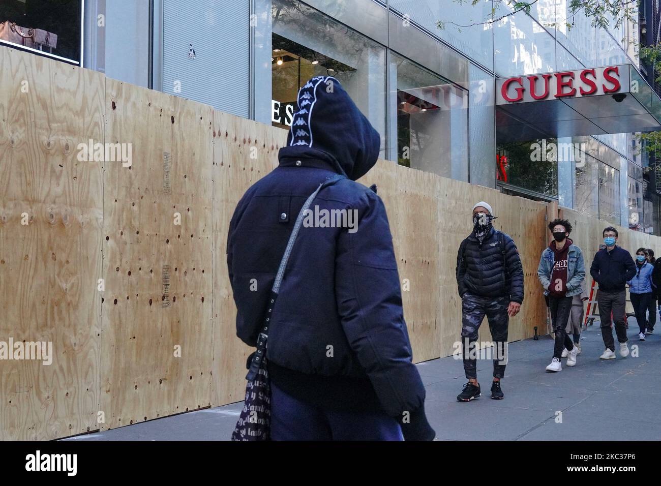 Maskierte Menschen kommen an einem Guess-Store vorbei, während Arbeiter in Erwartung der Unruhen im Zusammenhang mit den Präsidentschaftswahlen am 2. November 2020 in New York City an Bord gehen. Grundstückseigentümer bereiten sich darauf vor, dass lokale und staatliche Beamte am Wahltag vor Gewalt im ganzen Land warnen. (Foto von John Nacion/NurPhoto) Stockfoto