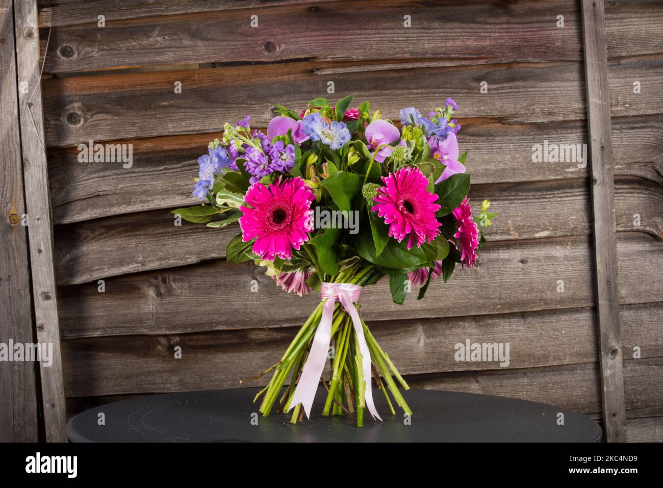 Ein farbenfroher Gerbera Blumenstrauß auf einem grauen Tisch mit Holzhintergrund Stockfoto