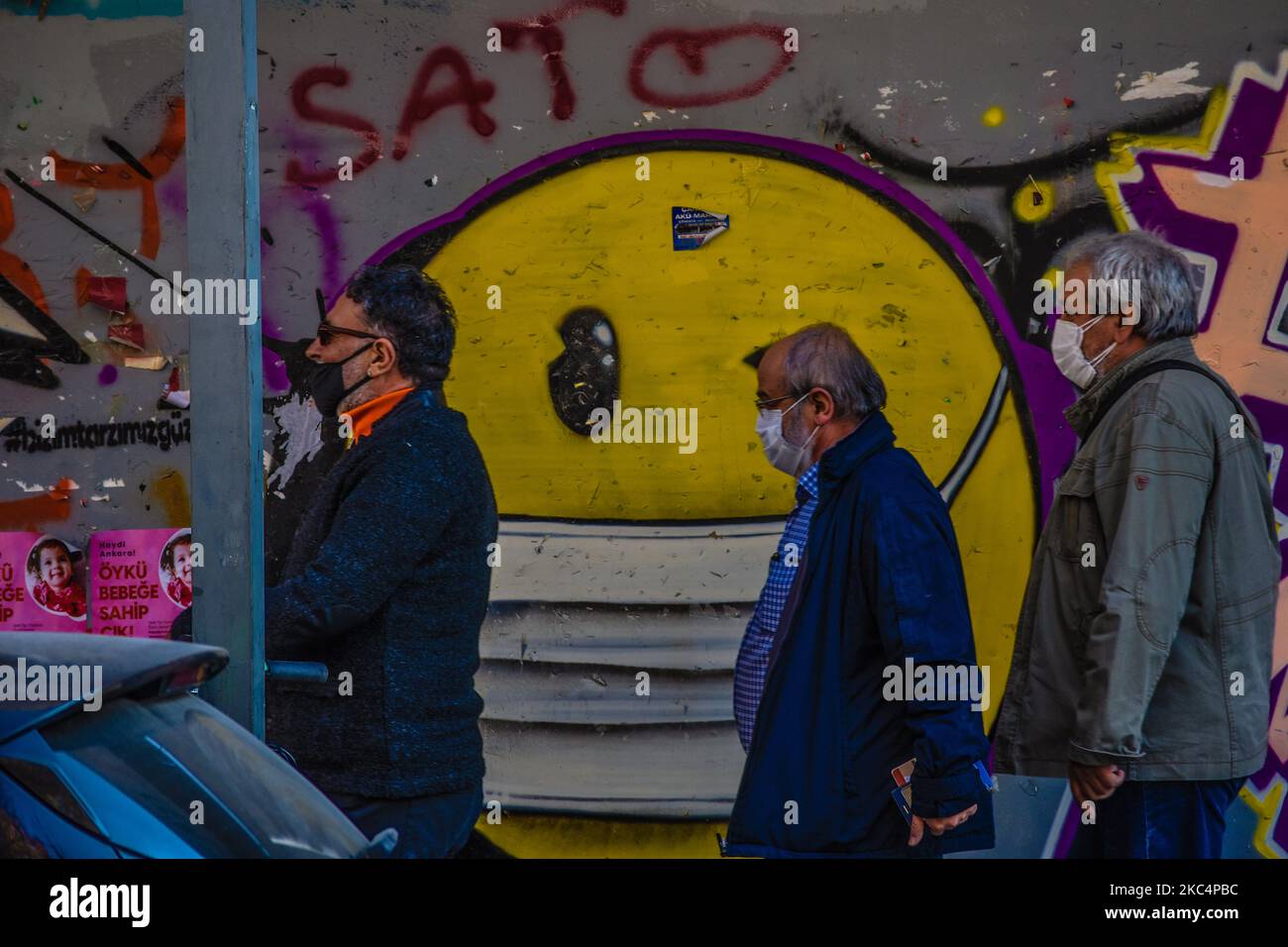 Drei Männer mit Schutzmaske gehen am 27. November 2020 in Ankara, Türkei, an einem Graffiti eines blinkenden Emojis mit Gesichtsmaske unter der Pandemie des Coronavirus (COVID-19) vorbei. (Foto von Altan Gocher/NurPhoto) Stockfoto