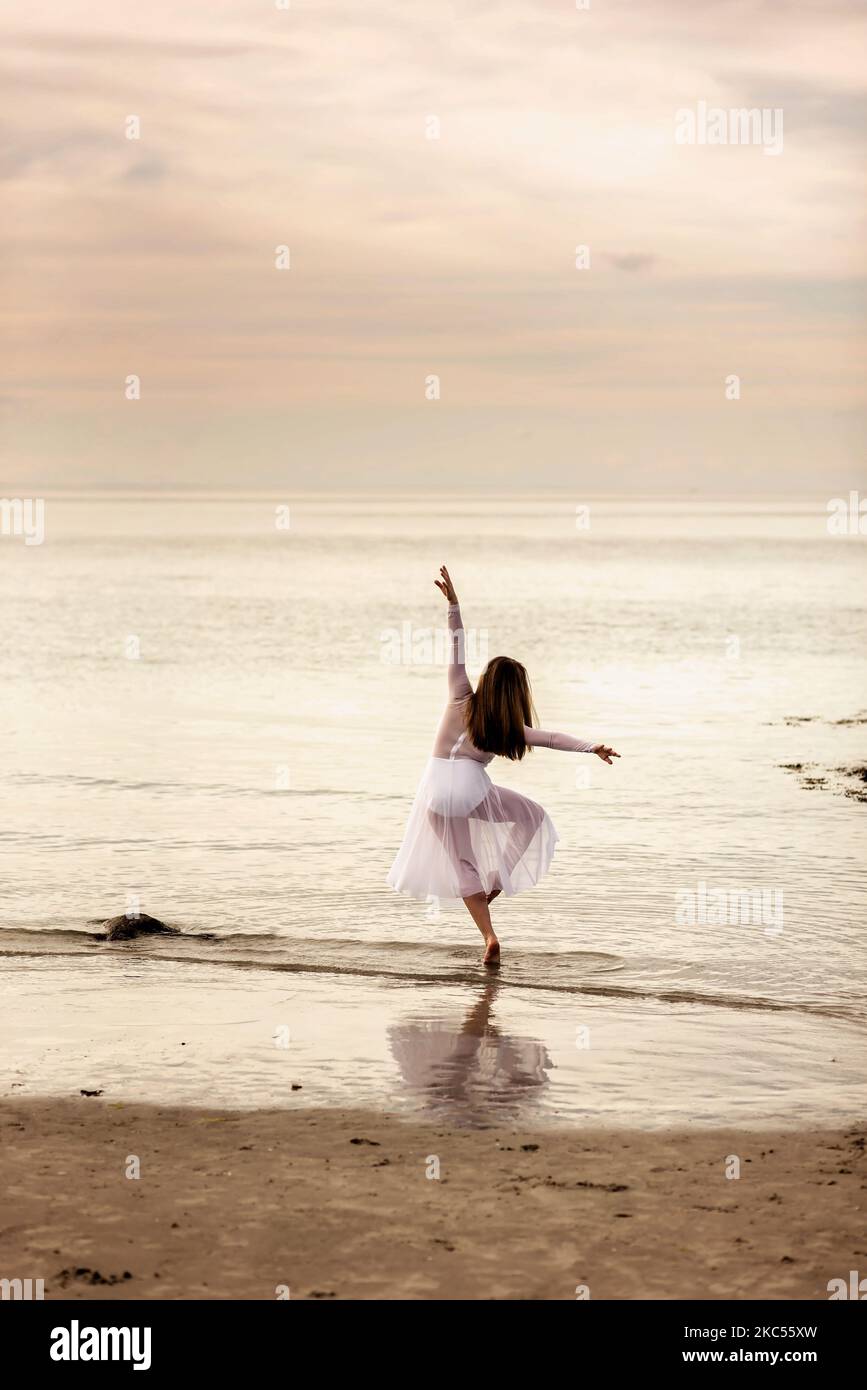 Eine Vertikale einer Tänzerin, die in einem durchscheinenden Kleid am Wingaersheek Beach, Massachusetts, posiert Stockfoto