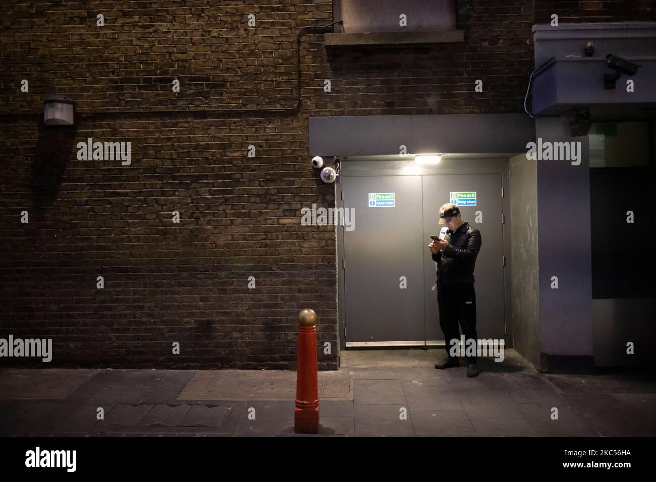 Soho Underworld, ein Mann auf seinem Smartphone unter gedämpfter Türbeleuchtung bei einer Winternacht in Soho, im Herzen des Londoner West End, England, Großbritannien Stockfoto