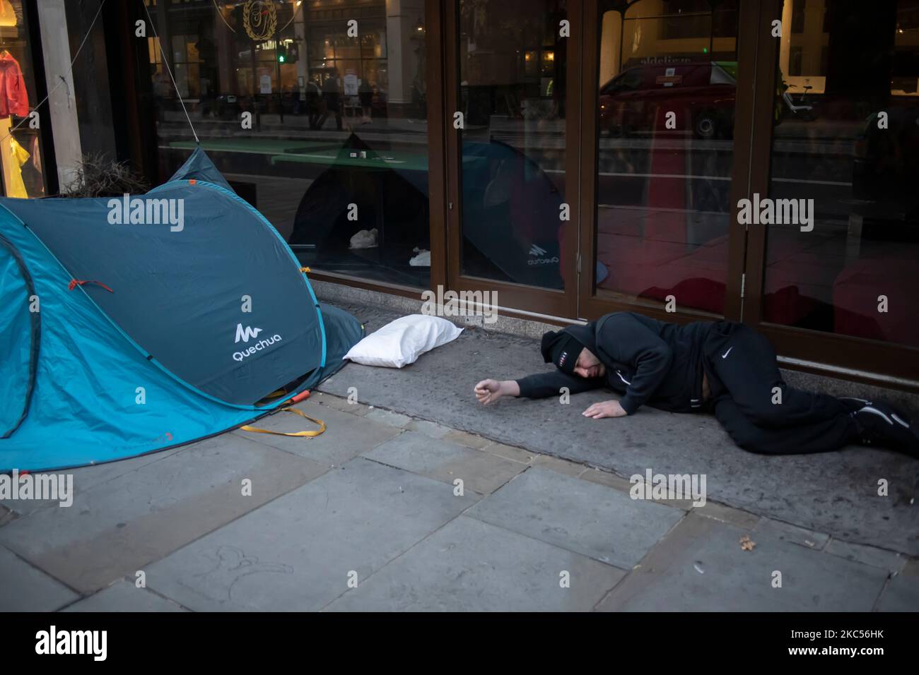 Obdachloser Einwanderer neben seinem Kissen und Zelt, der sich vor einem Restaurant auf dem Bürgersteig im Zentrum von London, England, Großbritannien, aufstellte Stockfoto