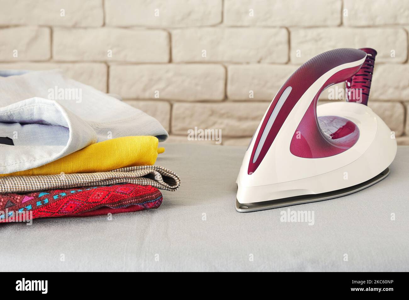 Modernes elektrisches Bügeleisen und Stapel gefalteter Kleidung auf dem Brett. Thema Hausarbeit und Wäscherei. Platz für Text kopieren Stockfoto