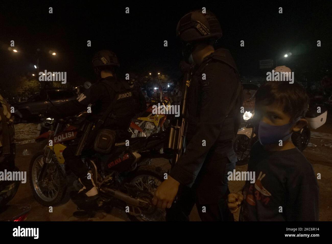 Ein Kind steht in der Nähe eines Mitglieds der indonesischen Polizei, das auf der Wache steht und Bewohner in der Menge um Silvester 2021 herum um die Ampera-Brücke, Palembang, am Donnerstag, den 31. Dezember 2021, zerstreut. (Foto von Sigit Prasetya/NurPhoto) Stockfoto