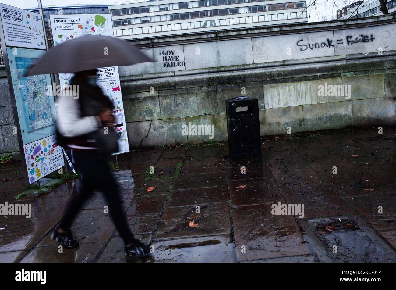 Eine Frau mit Gesichtsmaske geht bei nassem Wetter am 5. Januar 2021 in London, England, an regierungsfeindlichen Graffiti an einer Wand vor dem St. Thomas's Hospital vorbei. England begann heute seine dritte nationale Sperre, wobei die Menschen im ganzen Land erneut angewiesen wurden, außer für spezielle Ausnahmen zu Hause zu bleiben, wobei die Schulen wieder geschlossen wurden, wie sie es bei der ersten Sperre im vergangenen Frühjahr taten. Die Verhängung dieser neuen Beschränkungen, die gestern Abend in einer Fernsehansprache des britischen Premierministers Boris Johnson angekündigt wurde, ist eine Reaktion auf die Besorgnis der Behörden, dass der National Health Service (NH) Stockfoto