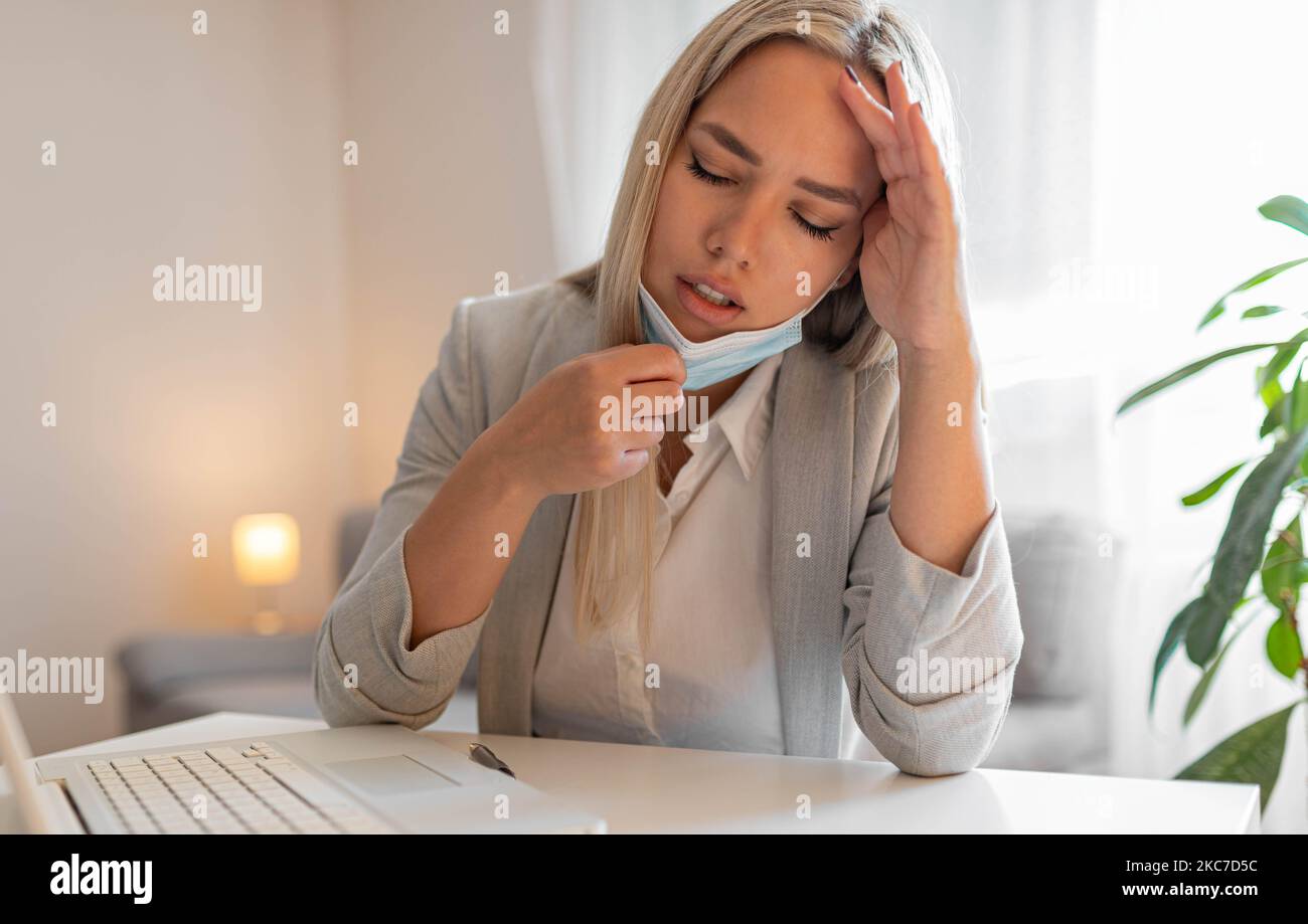 Frau, die im Büro arbeitet und Schwierigkeiten hat, mit Gesichtsmaske zu atmen, zieht die Maske nach unten.die Frau musste die Maske entfernen, um zu atmen Stockfoto