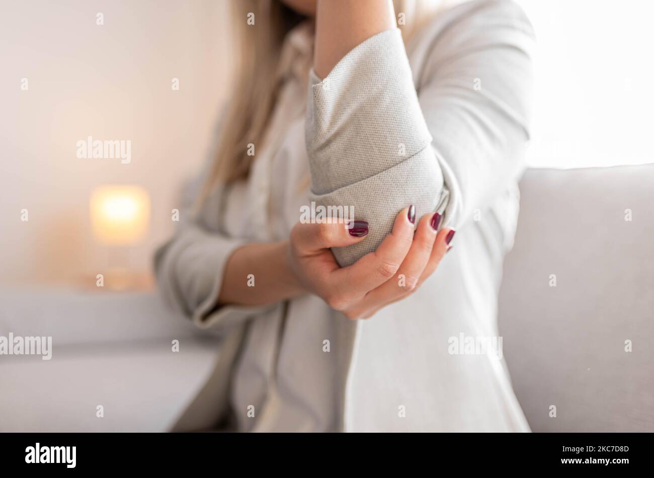 Frau mit Armschmerzen. Frau massiert schmerzhafte Hand drinnen. Frau, die ihren Ellenbogen in der Hand hält und unter Ellenbogenschmerzen leidet. Frau, die unter Schmerzen in der Hand leidet Stockfoto