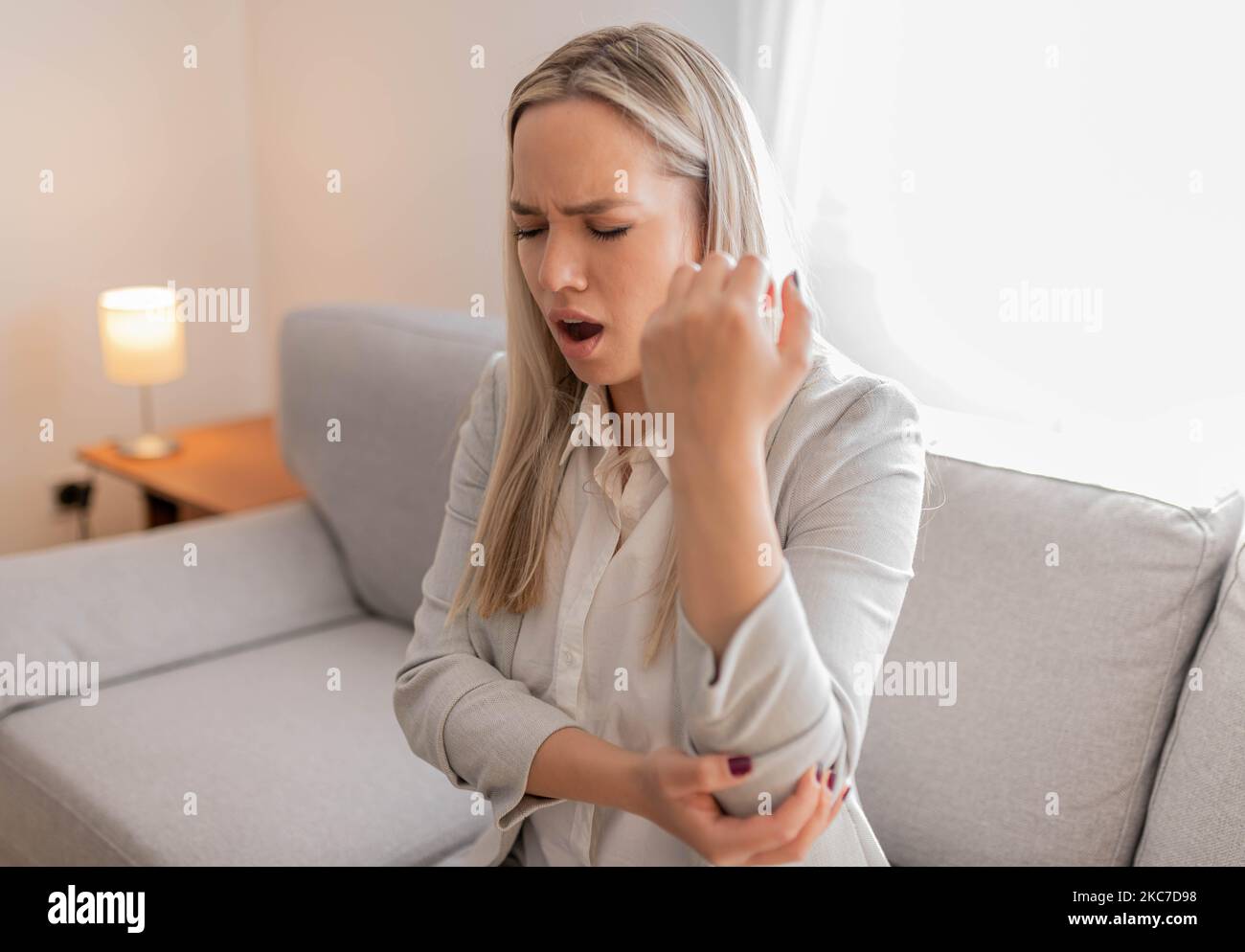 Frau mit Armschmerzen. Frau massiert schmerzhafte Hand drinnen. Frau, die ihren Ellenbogen in der Hand hält und unter Ellenbogenschmerzen leidet. Frau, die unter Schmerzen in der Hand leidet Stockfoto