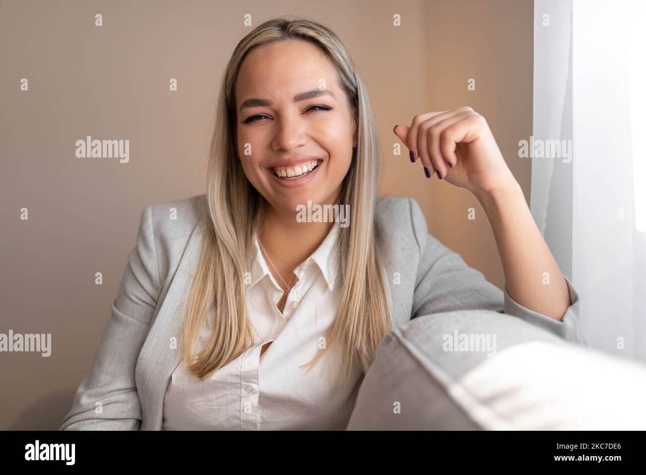 Glückliche junge Frau, die zu Hause auf dem Sofa sitzt und die Kamera anschaut. Porträt einer bequemen Frau, die sich auf dem Sessel entspannt. Porträt des schönen Mädchen Stockfoto