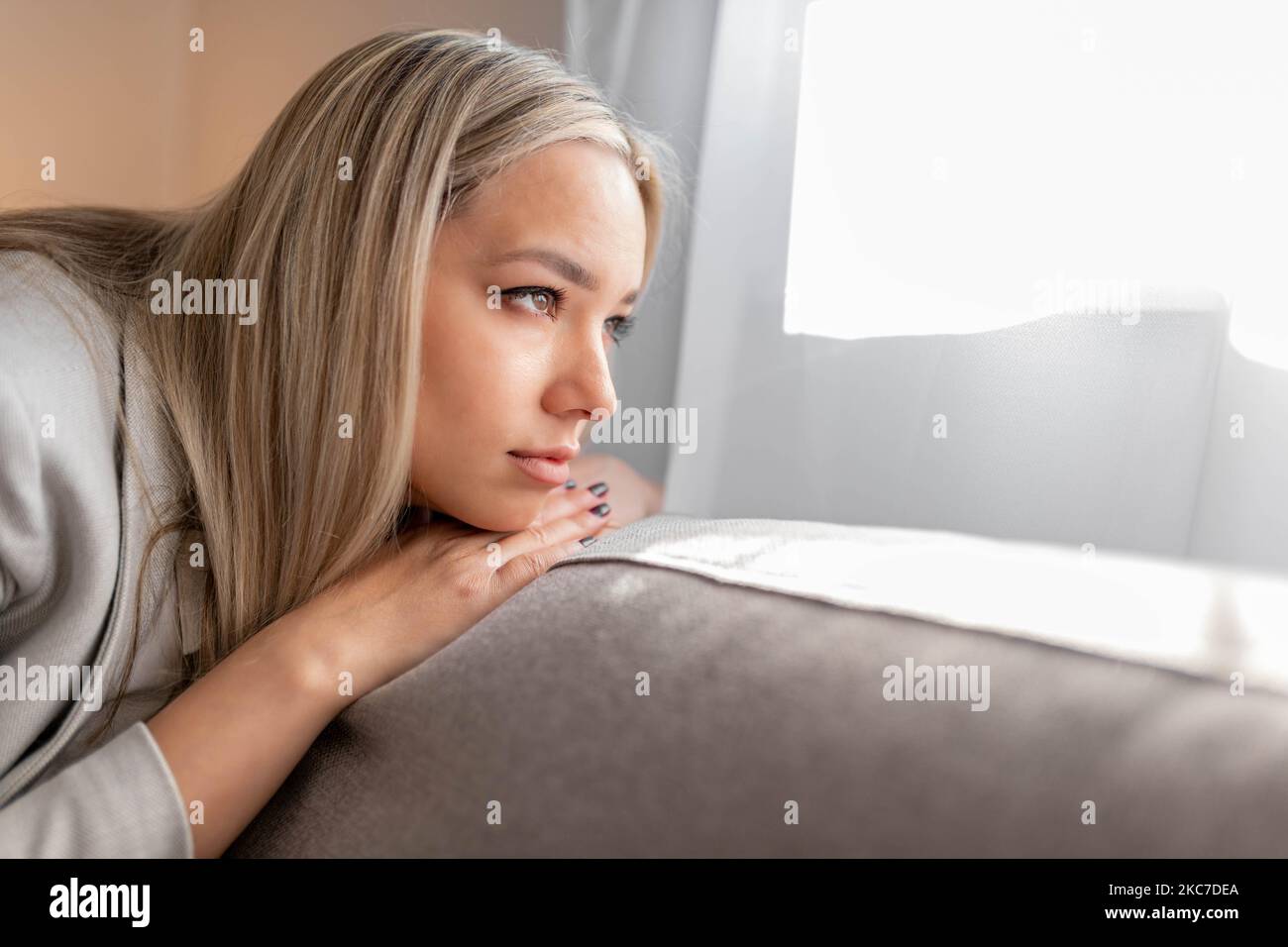 Traurige und deprimierte Frau, die auf dem Sofa sitzt und in die Ferne