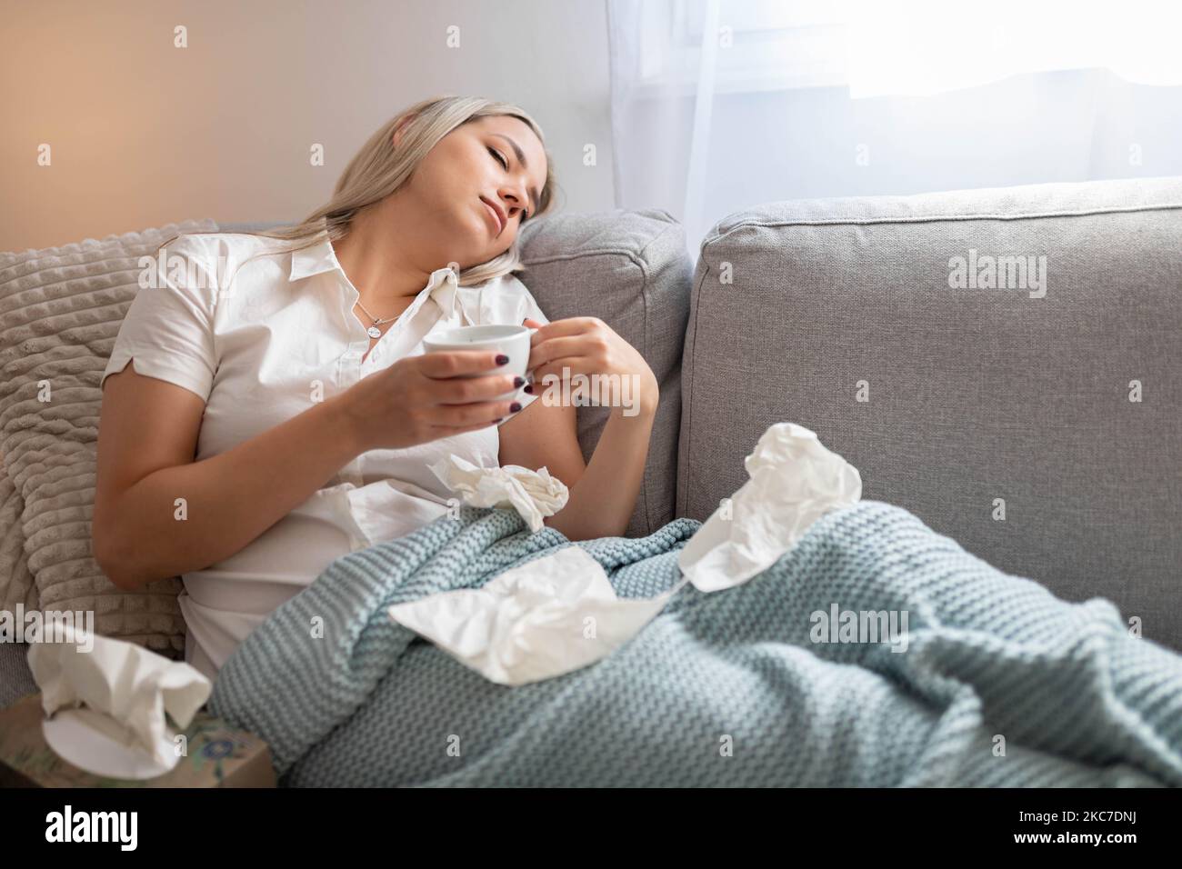 Kranke Frau, die unter der Decke sitzt. Kranke Frau mit saisonalen Infektionen, Grippe, Allergie im Bett liegend. Kranke Frau, die mit einer Decke im Bett lag Stockfoto