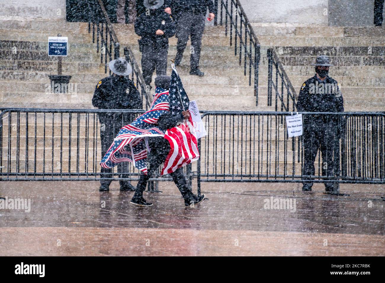 Ein Mann, der in US-Flaggen gehüllt ist, geht vor Polizeibeamten des Staates Ohio hin und her, die während eines bewaffneten Protestes vor der Amtseinführung des designierten Präsidenten Joe Biden im Gefolge der Coronavirus COVID-19-Pandemie am Sonntag, den 17.. Januar 2021 in Columbus Wache stehen. Ohio, Usa. (Foto von Jason Whitman/NurPhoto) Stockfoto