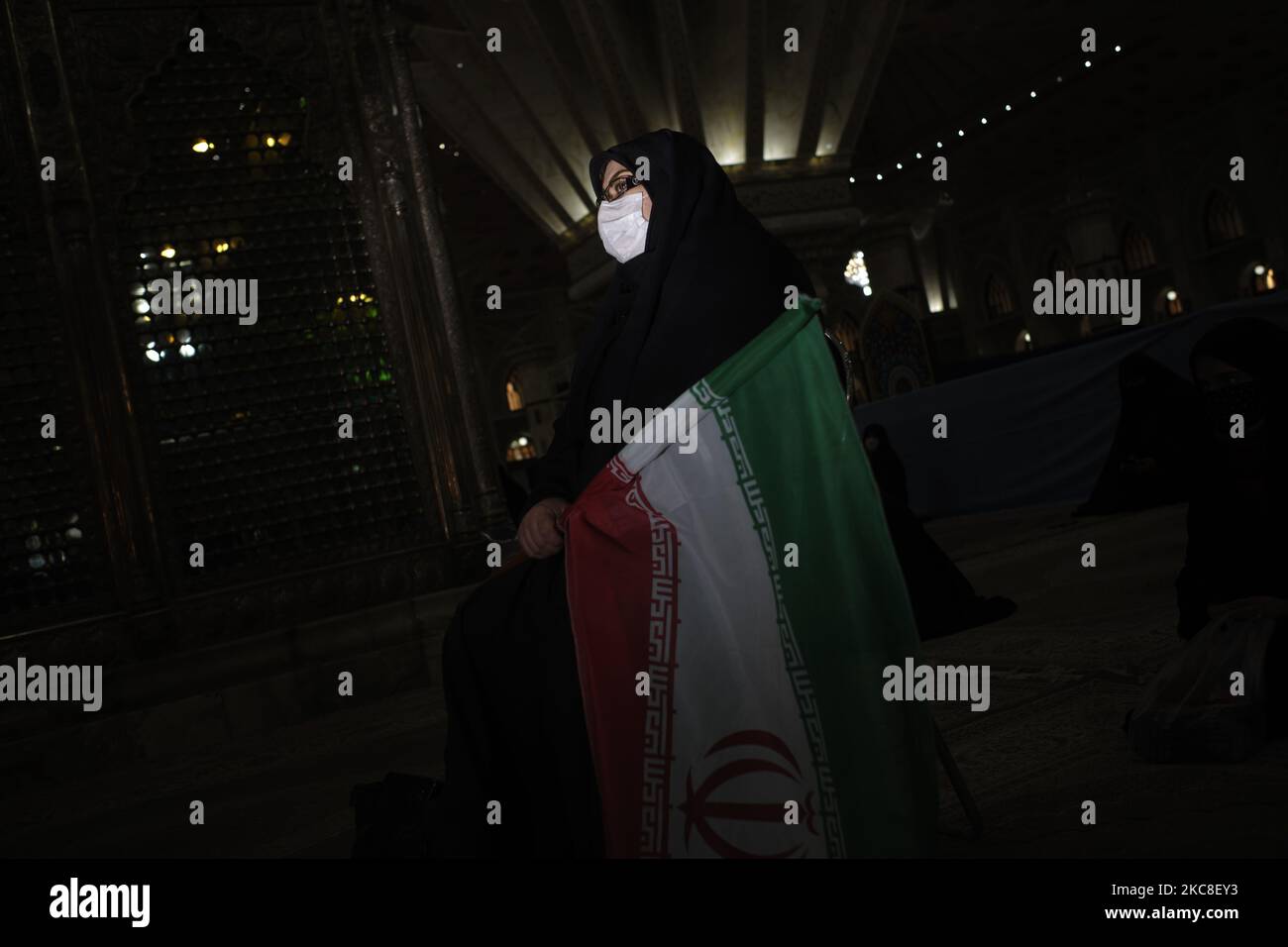 Eine verschleierte iranische Frau mit einer schützenden Gesichtsmaske hält eine iranische Flagge, während sie am ersten Tag des Sieges des Jahrestages der Islamischen Revolution auf dem Friedhof Behesht-e Zahra im Süden Teherans inmitten des COVID-19 neben dem Grab des verstorbenen iranischen Führers Ayatollah Ruhollah Khomeini sitzt Ausbruch im Iran am 31. Januar 2021. Der Iran feiert zehn Tage nach dem heutigen Tag den 42.. Jahrestag des Sieges der Islamischen Revolution, aber der Ausbruch der neuen Coronavirus-Krankheit (COVID-19) hat die diesjährigen Feierlichkeiten nicht wie in den vergangenen Jahren gefeiert. (Foto von Morteza Nikoubazl/NurPhoto) Stockfoto