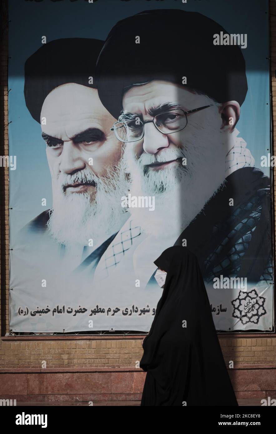 Eine verschleierte iranische Frau mit einer schützenden Gesichtsmaske geht an Porträts des verstorbenen iranischen Führers Ayatollah Ruhollah Khomeini (L) und des Obersten Führers Ayatollah Ali Khamenei vorbei, als sie am ersten Tag der zehntägigen Feier zum Jahrestag des Sieges der Islamischen Revolution teilnimmt. Auf dem Friedhof Behesht-e Zahra im Süden Teherans, inmitten des COVID-19-Ausbruchs im Iran am 31. Januar 2021. Der Iran feiert in zehn Tagen den 42.. Jahrestag des Sieges der Islamischen Revolution, aber der Ausbruch der neuen Coronavirus-Krankheit (COVID-19) hat in diesem Jahr nicht gefeiert Stockfoto