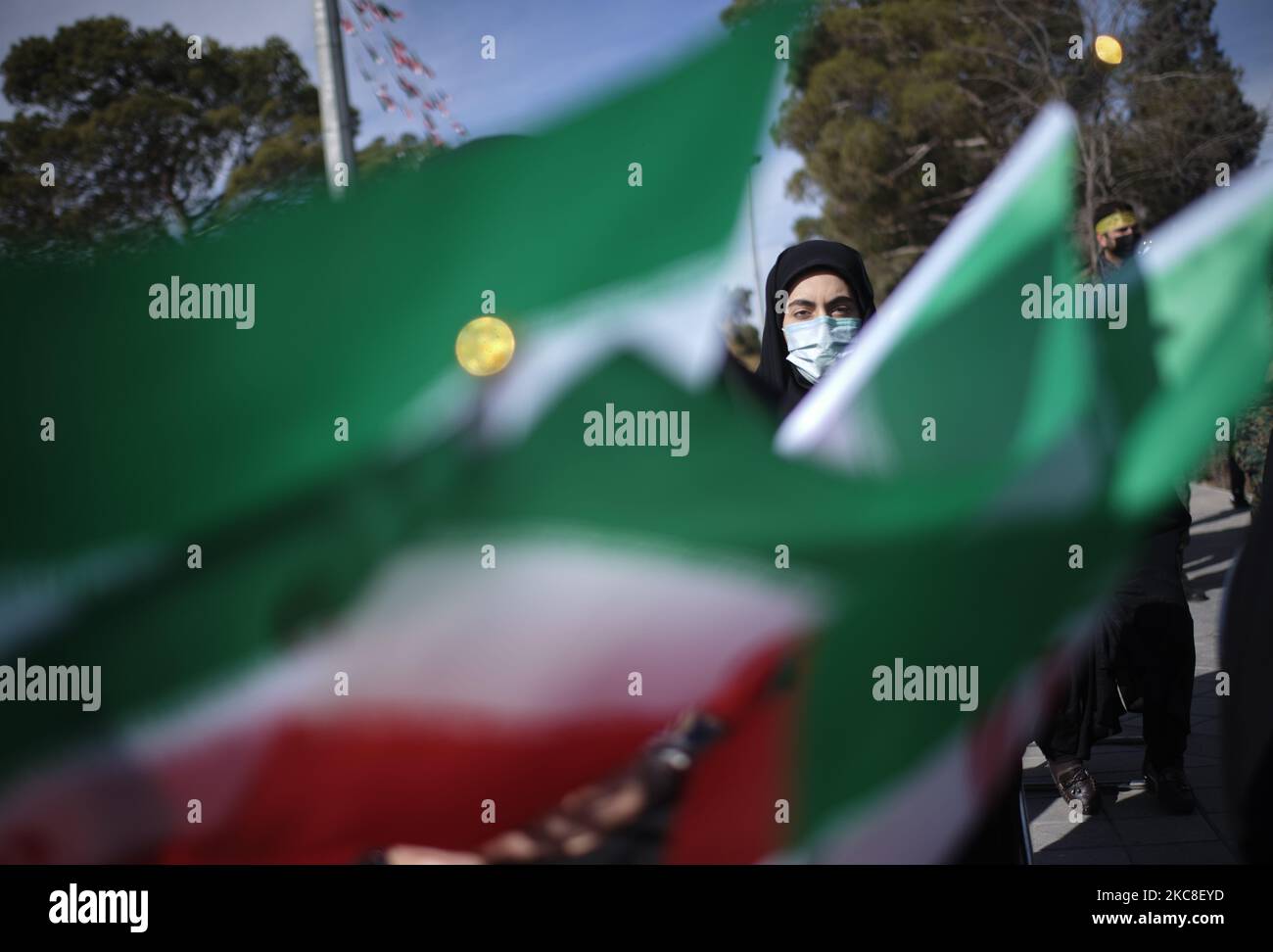 Eine verschleierte iranische Frau, die eine schützende Gesichtsmaske trägt, sieht auf, als sie hinter den iranischen Flaggen sitzt, während sie am ersten Tag der zehntägigen Feier zum Jahrestag des Sieges der Islamischen Revolution teilnimmt. Auf dem Friedhof Behesht-e Zahra im Süden Teherans, inmitten des COVID-19-Ausbruchs im Iran am 31. Januar 2021. Der Iran feiert zehn Tage nach dem heutigen Tag den 42.. Jahrestag des Sieges der Islamischen Revolution, aber der Ausbruch der neuen Coronavirus-Krankheit (COVID-19) hat die diesjährigen Feierlichkeiten nicht wie in den vergangenen Jahren gefeiert. (Foto von Morteza Nikoubazl/NurPhoto) Stockfoto