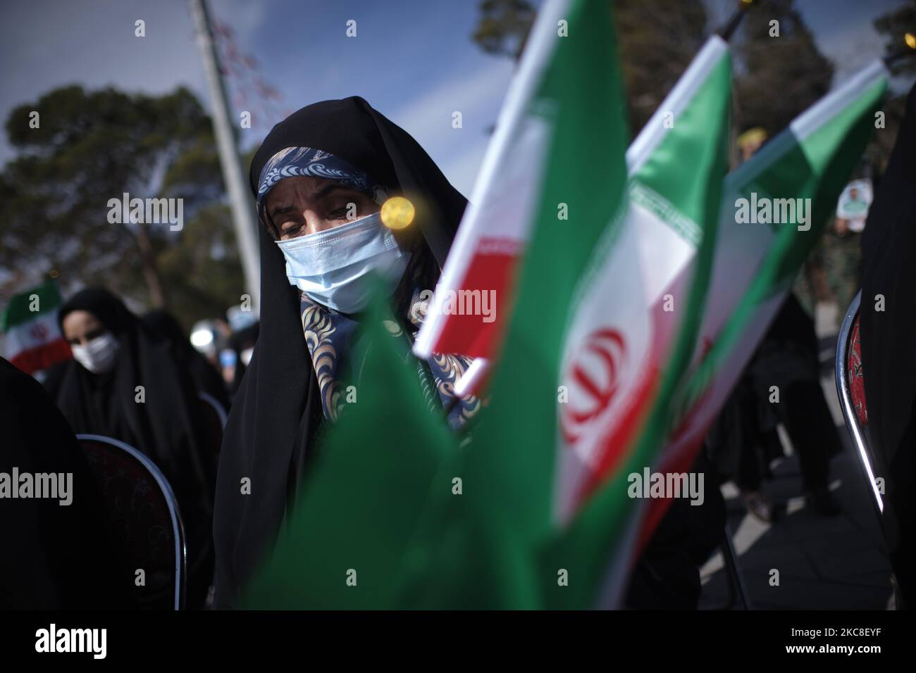 Eine verschleierte iranische Frau, die eine Schutzmaske trägt, hält am ersten Tag der zehntägigen Feier zum Jahrestag des Sieges der Islamischen Revolution auf dem Friedhof Behesht-e Zahra im Süden Teherans inmitten des COVID-19-Ausbruchs im Iran am 31. Januar 2021 iranische Flaggen fest. Der Iran feiert zehn Tage nach dem heutigen Tag den 42.. Jahrestag des Sieges der Islamischen Revolution, aber der Ausbruch der neuen Coronavirus-Krankheit (COVID-19) hat die diesjährigen Feierlichkeiten nicht wie in den vergangenen Jahren gefeiert. (Foto von Morteza Nikoubazl/NurPhoto) Stockfoto