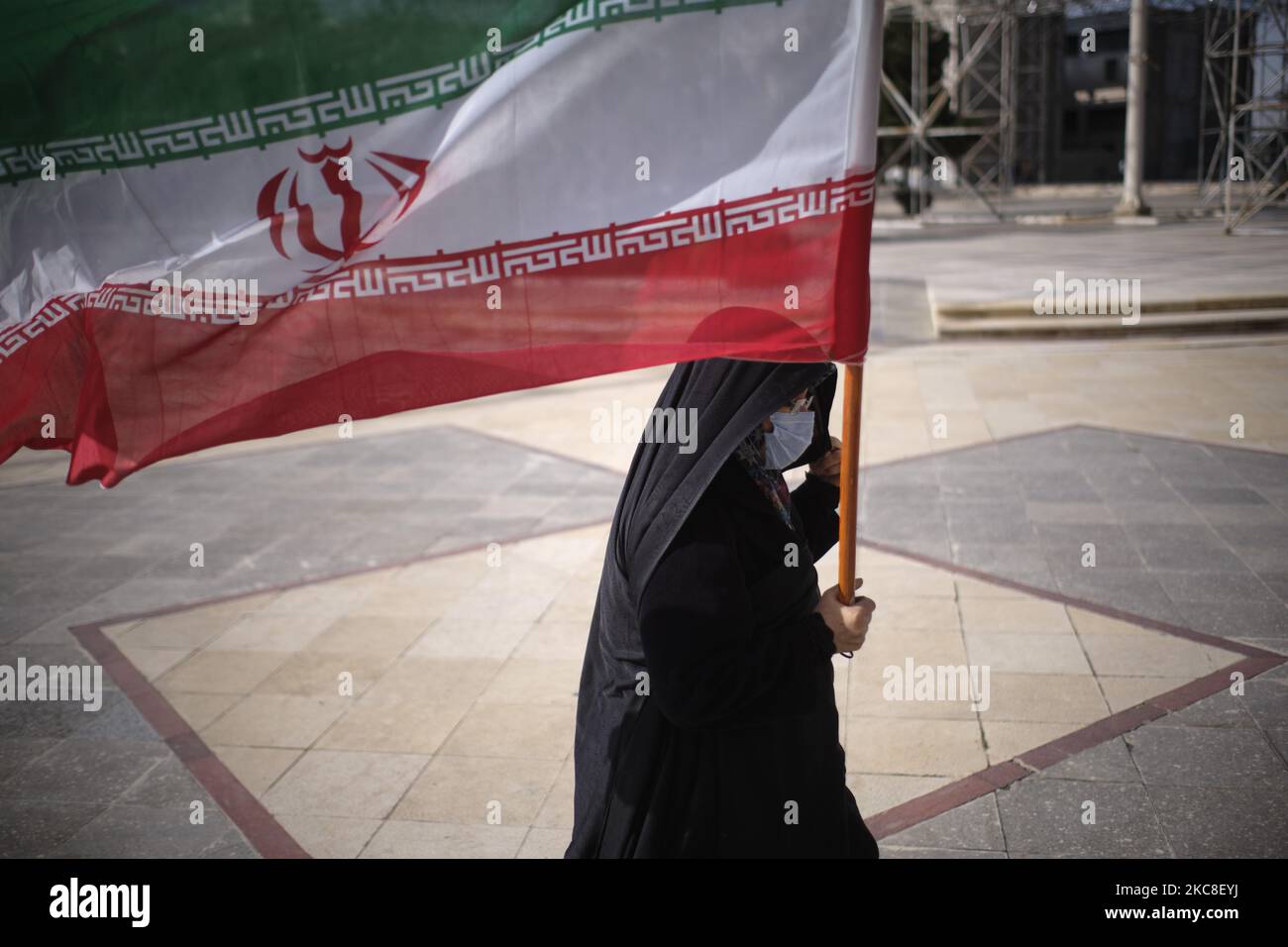 Eine verschleierte iranische Frau, die eine schützende Gesichtsmaske trägt, die eine iranische Flagge trägt, während sie am ersten Tag des Sieges des Jahrestages der Islamischen Revolution auf dem Friedhof Behesht-e Zahra im Süden Teherans inmitten eines Bereichs im Heiligtum des verstorbenen iranischen Führers Ayatollah Ruhollah Khomeini spaziert Der COVID-19-Ausbruch im Iran am 31. Januar 2021. Der Iran feiert zehn Tage nach dem heutigen Tag den 42.. Jahrestag des Sieges der Islamischen Revolution, aber der Ausbruch der neuen Coronavirus-Krankheit (COVID-19) hat die diesjährigen Feierlichkeiten nicht wie in den vergangenen Jahren gefeiert. (Foto von Morteza Nikoubazl/NurPh Stockfoto