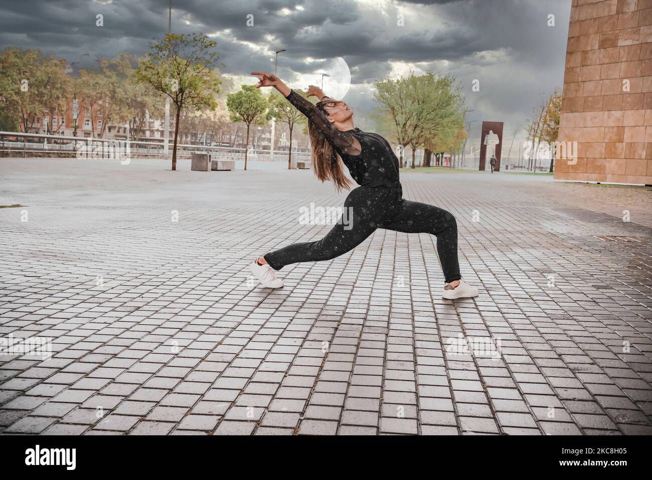 Blonde junge Frau in schwarzem Kleid, die im Regen auf der Straße tanzt. Tanzkonzept Stockfoto