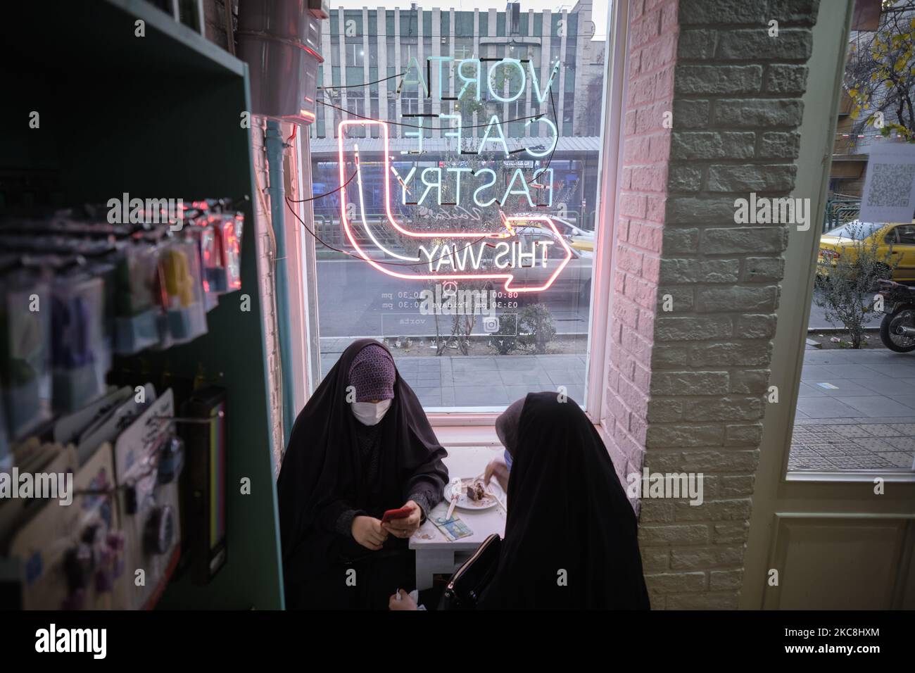 Zwei verschleierte iranische Frauen sitzen in einem Café in der Enghelab (Revolution) Avenue im Zentrum von Teheran während der zehntägigen Feierlichkeiten zum 42. Jahrestag des Sieges der Islamischen Revolution im Iran am 1. Februar 2021. (Foto von Morteza Nikoubazl/NurPhoto) Stockfoto