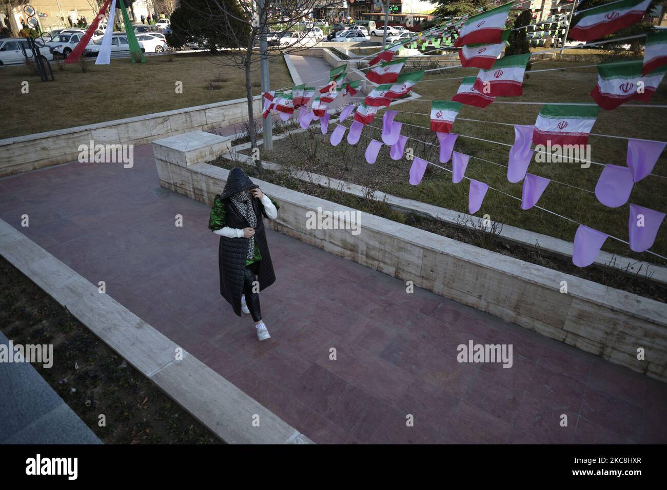 Als Reaktion auf die Kamera verbirgt eine iranische Frau ihr Gesicht mit ihrem Kopftuch, während sie auf dem Vanak-Platz, der mit iranischen Flaggen geschmückt ist, während der zehntägigen Feierlichkeiten zum 42. Jahrestag des Sieges der iranischen Islamischen Revolution am 1. Februar 2021 im Norden Teherans spaziert. (Foto von Morteza Nikoubazl/NurPhoto) Stockfoto