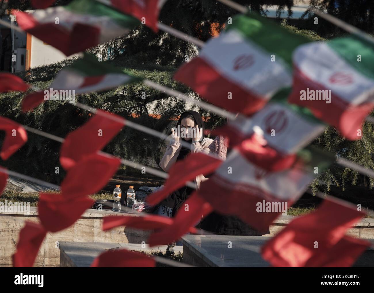 Eine Iranerin passt ihr Kopftuch an, während sie auf einem Platz sitzt, der mit Iran-Flaggen geschmückt ist, während der zehntägigen Feierlichkeiten zum 42. Jahrestag des Sieges der Islamischen Revolution im Iran am 1. Februar 2021 im Norden Teherans. (Foto von Morteza Nikoubazl/NurPhoto) Stockfoto