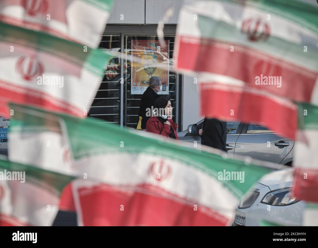 Eine iranische Frau schaut zu, während sie auf einer Ecke eines Platzes steht, der mit iranischen Flaggen geschmückt ist, während der zehntägigen Feierlichkeiten zum 42. Jahrestag des Sieges der Islamischen Revolution im Iran am 1. Februar 2021 im Norden Teherans. (Foto von Morteza Nikoubazl/NurPhoto) Stockfoto