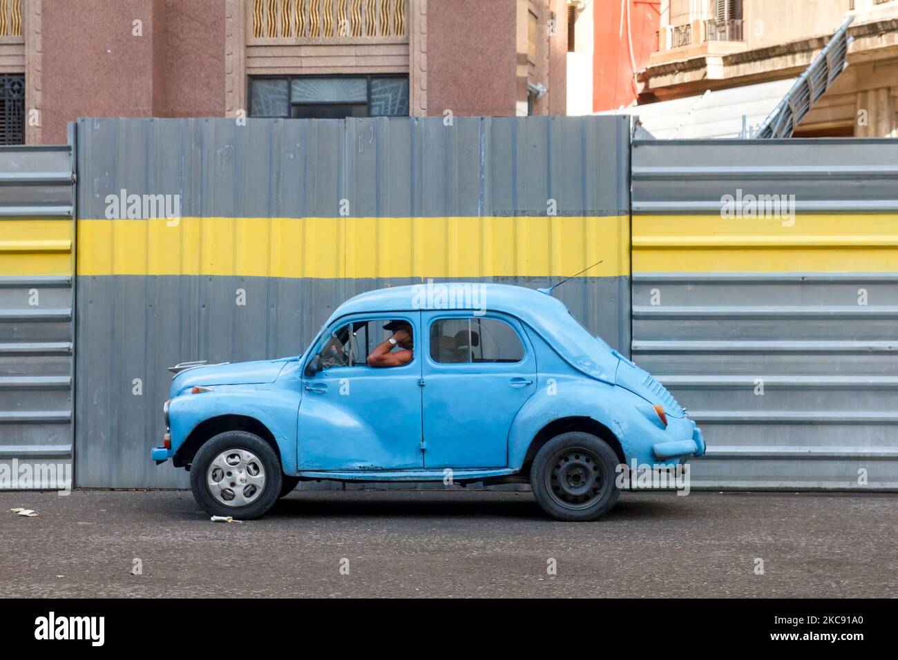 Ein altes, veraltetes Auto wird an einem metallischen Zaun eines Gebäudes geparkt, das gerade umgebaut wird. Stockfoto