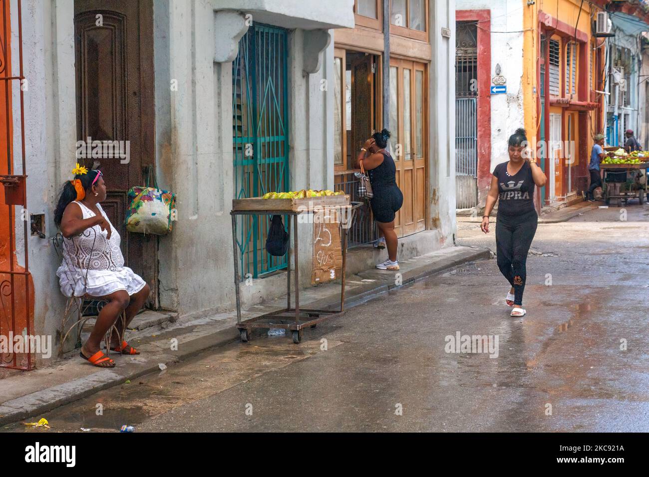 Kubaner in einer nassen Straße. Es gibt einen rustikalen Wagen eines Verkäufers, der Früchte verkauft. Stockfoto