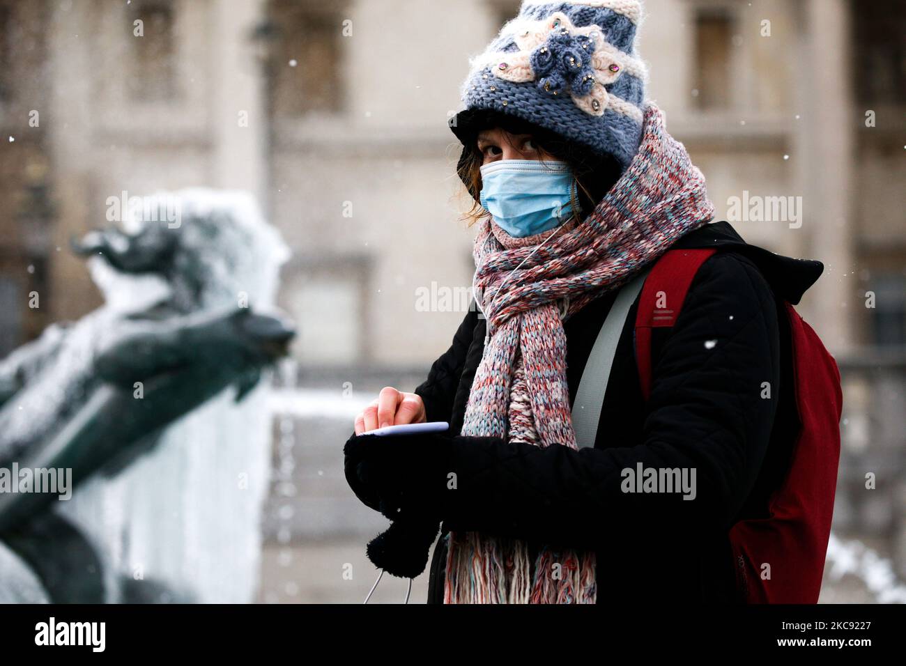 Eine Frau mit Gesichtsmaske steht am 9. Februar 2021 in der Nähe einer gefrorenen Statue in einem der Brunnen des Trafalgar Square in London, England. Das Vereinigte Königreich spürt weiterhin die kalten Wettereffekte des Sturms Darcy, der dem Land mehrere Tage Schnee und Bedingungen unter Null gebracht hat. (Foto von David Cliff/NurPhoto) Stockfoto