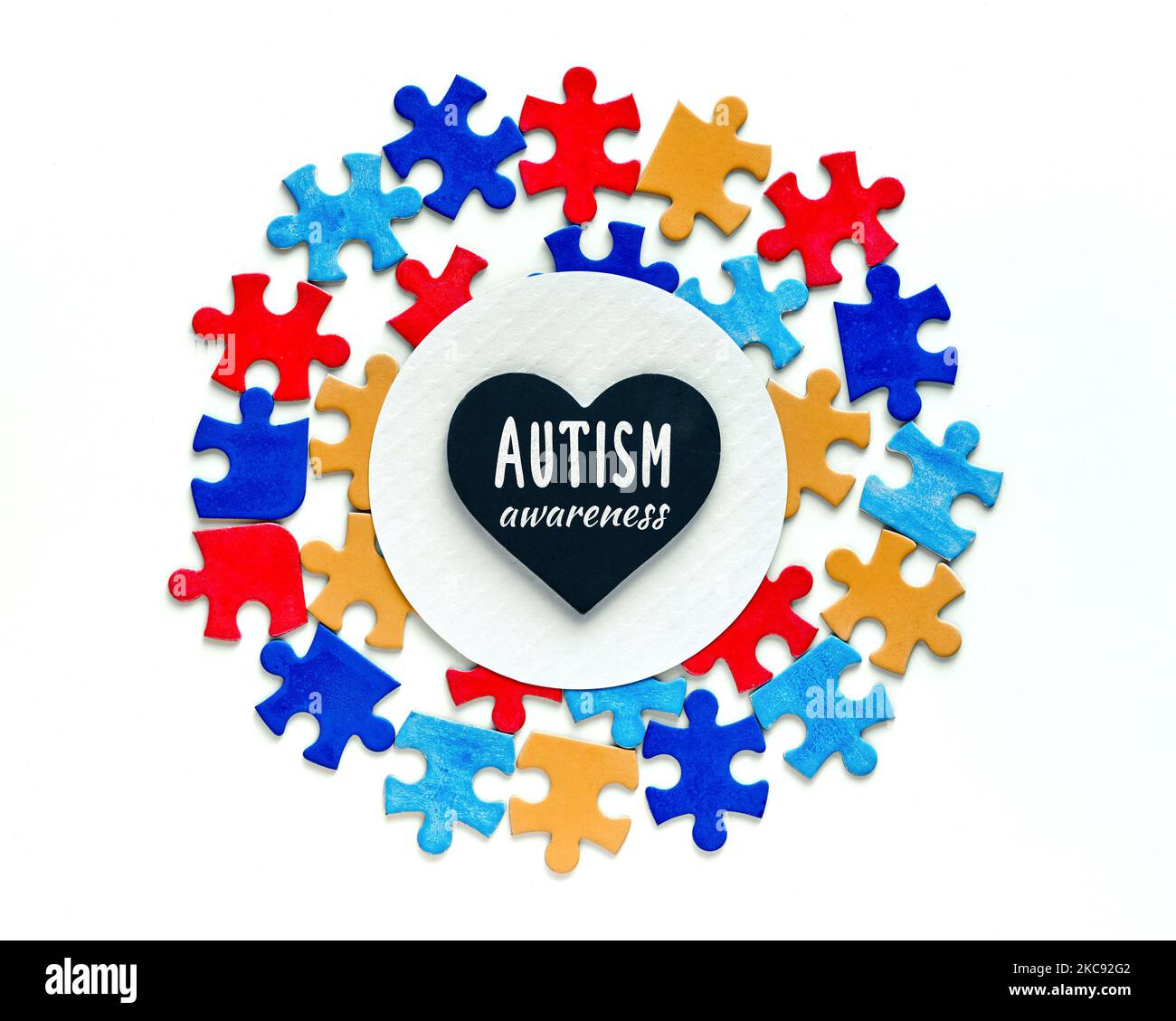 Text zur Autismus-Wahrnehmung auf schwarzem Herzen, herzförmiger Tafel, Kreidetafel auf weißem Papierkreis, eingerahmt von Puzzleteilen. Symbol für Autismus-Bewusstsein Stockfoto