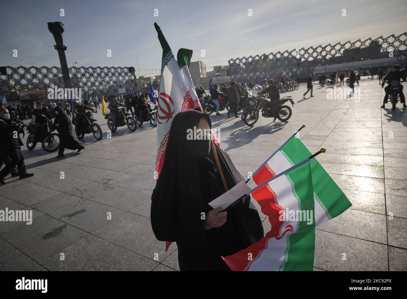 Eine verschleierte iranische Frau mit Schutzmaske hält Iran-Flaggen bei einer Kundgebung zum Gedenken an den 42.. Jahrestag des Sieges der Islamischen Revolution, die am 10. Februar 2021 auf dem Imam-Hussein-Platz im Süden Teherans mit Motorrädern inmitten des Ausbruchs der neuen Coronavirus-Krankheit (COVID-19) im Iran stattfand. (Foto von Morteza Nikoubazl/NurPhoto) Stockfoto