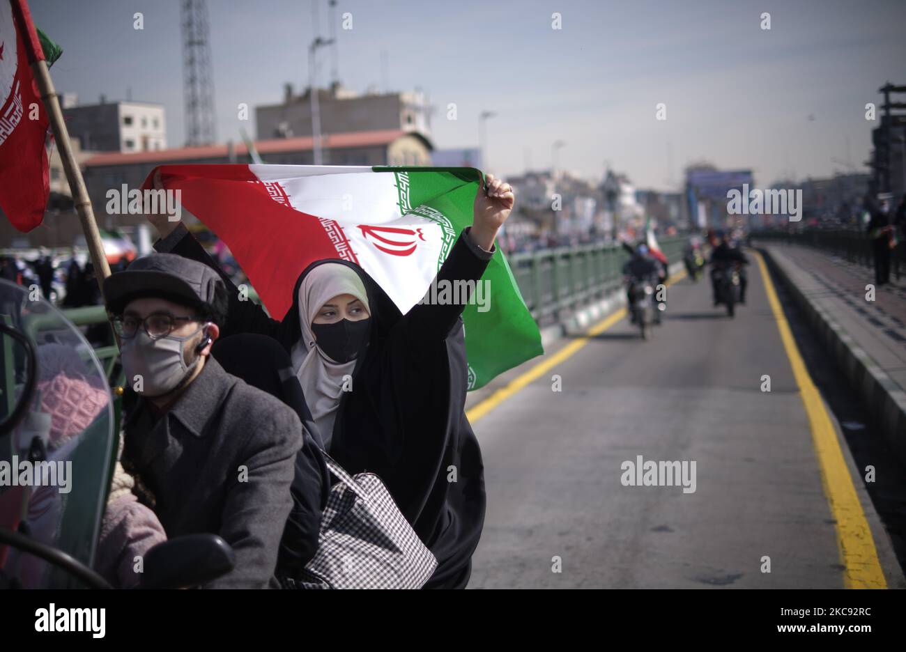 Eine verschleierte iranische Frau schwingt eine iranische Flagge, während ihr Mann während einer Kundgebung zum Gedenken an den Sieg der Islamischen Revolution 42. mit dem Motorrad auf der Azadi-Straße (Freedom) fährt. Das fand am 10. Februar 2021, am 10. Februar 2021, in Teheran mit Motorrädern unter dem Ausbruch der neuen Coronavirus-Krankheit (COVID-19) im Iran statt. (Foto von Morteza Nikoubazl/NurPhoto) Stockfoto