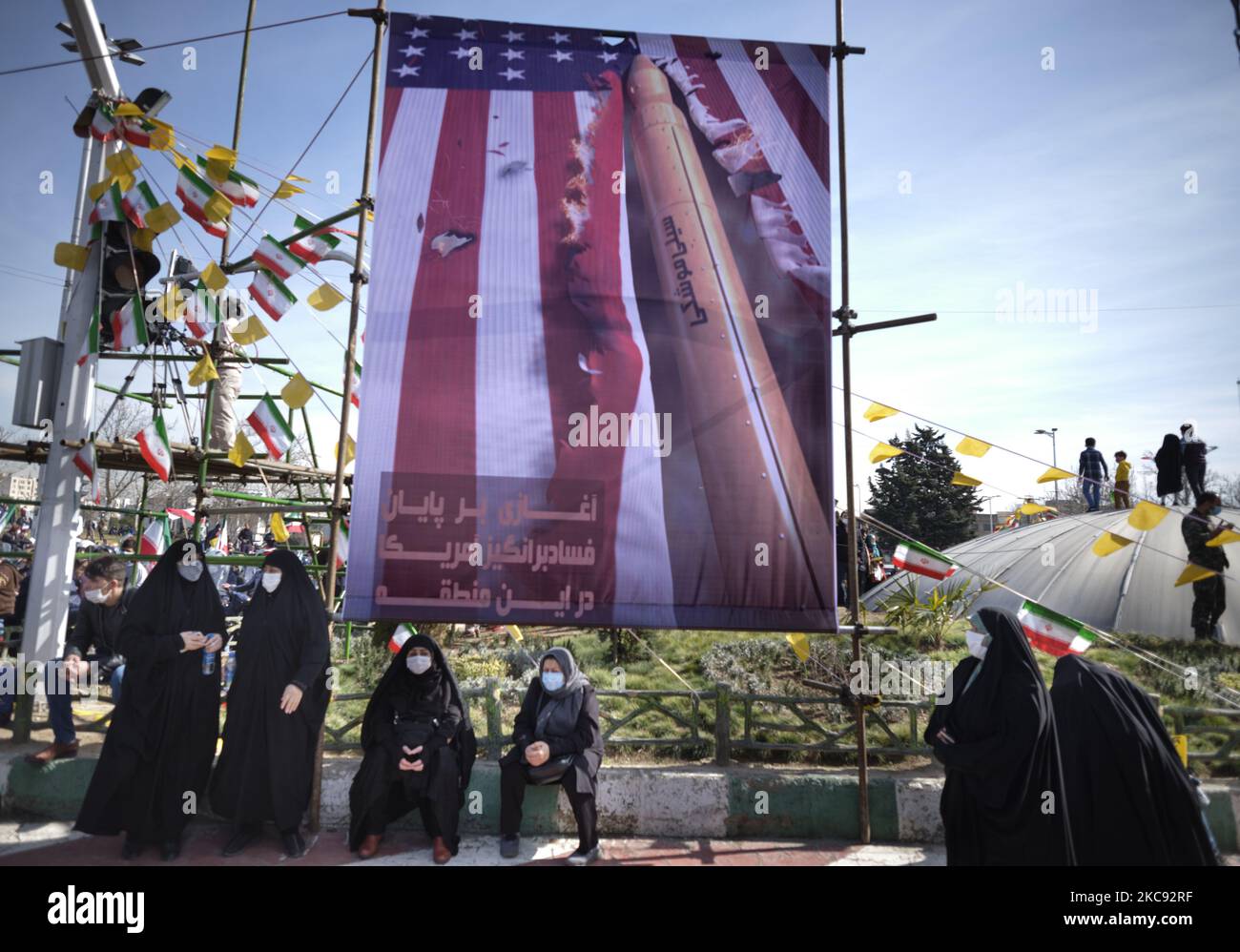 Iranische verschleierte Frauen unter einem Anti-USA-Banner auf dem Platz der Freiheit (Azadi) während einer Kundgebung zum Gedenken an den 42.. Jahrestag des Sieges der Islamischen Revolution, die am 10. Februar 2021, am 10. Februar 2021, mit Motorrädern, inmitten des Ausbruchs der neuen Coronavirus-Krankheit (COVID-19) im Iran stattfand. (Foto von Morteza Nikoubazl/NurPhoto) Stockfoto
