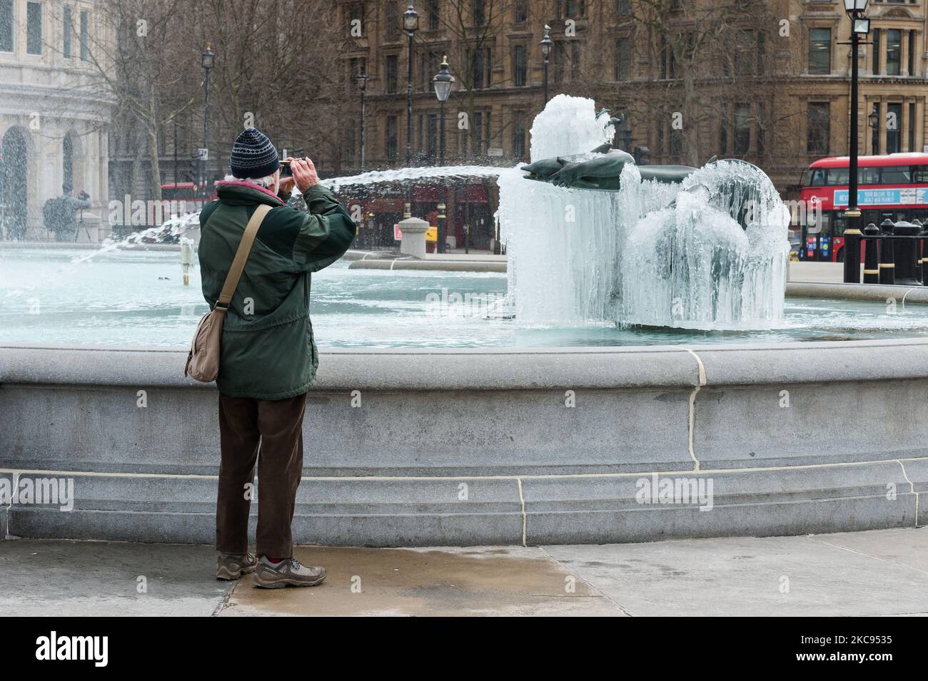 Ein Mann macht am 12. Februar 2021 in London, England, ein Foto einer gefrorenen Meerjungfrau-Statue im Brunnen am Trafalgar Square an einem kalten Wintertag, an dem England unter der dritten Sperre bleibt, um die Covid-19-Infektionsraten zu reduzieren. (Foto von Wiktor Szymanowicz/NurPhoto) Stockfoto