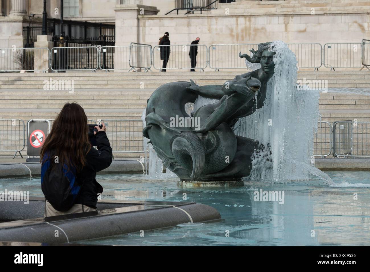 Eine Frau macht am 12. Februar 2021 in London, England, ein Foto einer gefrorenen Meerjungfrau-Statue im Brunnen am Trafalgar Square an einem kalten Wintertag, an dem England noch unter der dritten Sperre steht, um die Covid-19-Infektionsraten zu senken. (Foto von Wiktor Szymanowicz/NurPhoto) Stockfoto
