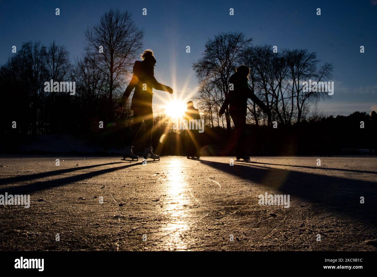Dunkle Silhouetten von Menschen beim Eislaufen auf dem kristallklaren natürlichen gefrorenen See in der Region Nordbrabant am Nachmittag vor dem Sonnenuntergang. Eislaufrausch übernimmt die Niederlande. Die Niederländer haben viel Spaß und genießen das einwöchige, kalte Schneewetter mit Temperaturen unter Null, die dazu führen, dass Seen, Bäche, Teiche, Flüsse und Kanäle gefrieren. Im Park Meerland in der Nähe der Stadt Eindhoven haben sich die Massen an einem sonnigen Tag mit blauem Himmel abgesetzt, da es eine niederländische Tradition ist. Außerdem werden die Menschen im Freien in der eisgefrorenen Natur und der kalten Umgebung gesehen, die auf dem Eis der gefrorenen Seen spazieren gehen, p Stockfoto