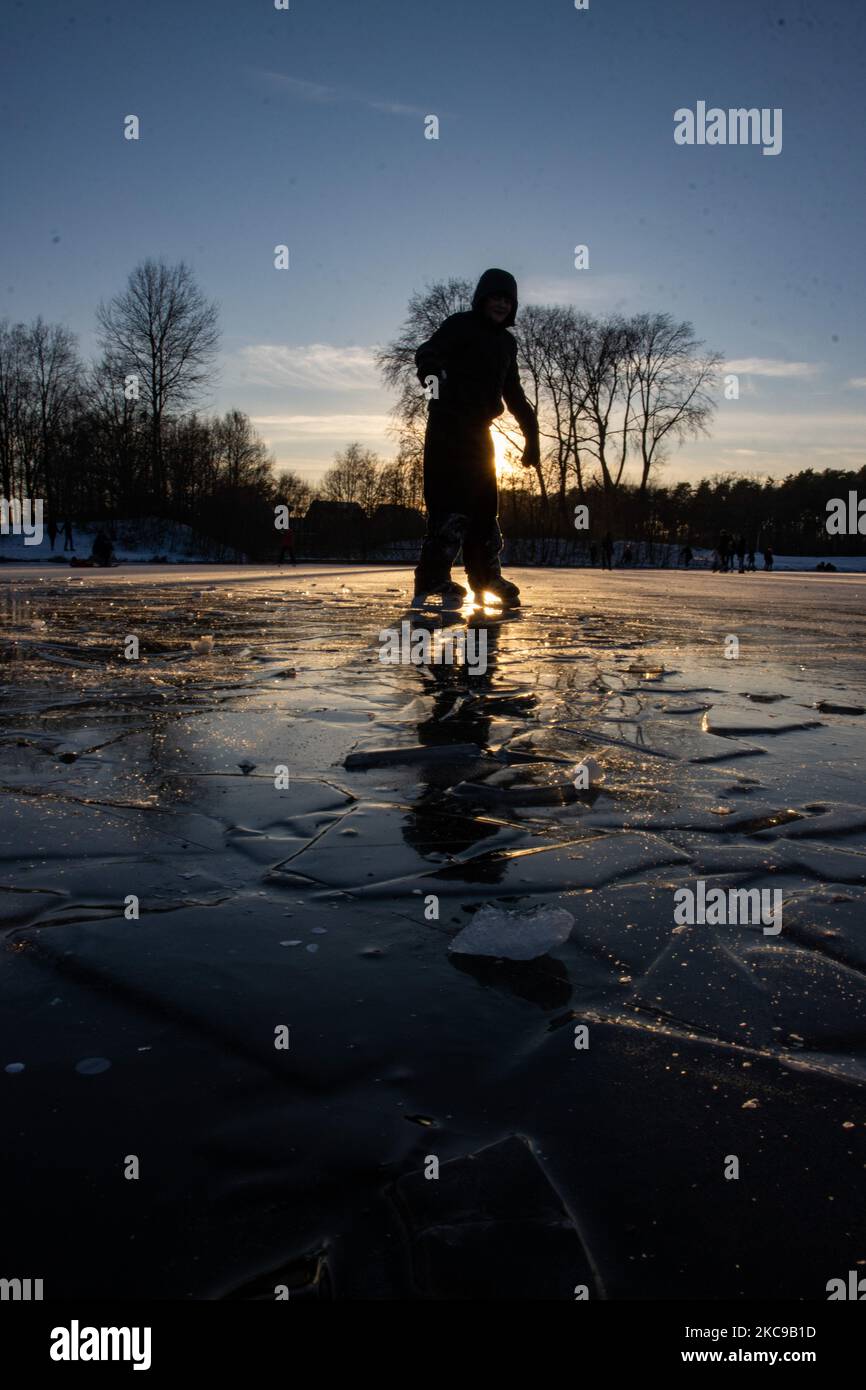 Dunkle Silhouetten von Menschen beim Eislaufen auf dem kristallklaren natürlichen gefrorenen See in der Region Nordbrabant am Nachmittag vor dem Sonnenuntergang. Eislaufrausch übernimmt die Niederlande. Die Niederländer haben viel Spaß und genießen das einwöchige, kalte Schneewetter mit Temperaturen unter Null, die dazu führen, dass Seen, Bäche, Teiche, Flüsse und Kanäle gefrieren. Im Park Meerland in der Nähe der Stadt Eindhoven haben sich die Massen an einem sonnigen Tag mit blauem Himmel abgesetzt, da es eine niederländische Tradition ist. Außerdem werden die Menschen im Freien in der eisgefrorenen Natur und der kalten Umgebung gesehen, die auf dem Eis der gefrorenen Seen spazieren gehen, p Stockfoto