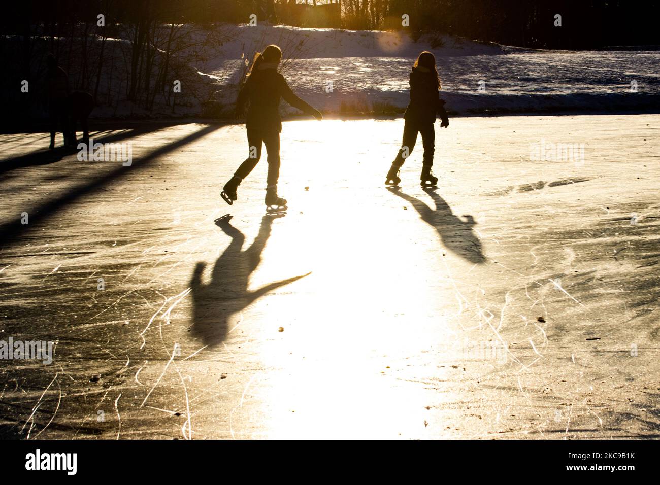 Dunkle Silhouetten von Menschen beim Eislaufen auf dem kristallklaren natürlichen gefrorenen See in der Region Nordbrabant am Nachmittag vor dem Sonnenuntergang. Eislaufrausch übernimmt die Niederlande. Die Niederländer haben viel Spaß und genießen das einwöchige, kalte Schneewetter mit Temperaturen unter Null, die dazu führen, dass Seen, Bäche, Teiche, Flüsse und Kanäle gefrieren. Im Park Meerland in der Nähe der Stadt Eindhoven haben sich die Massen an einem sonnigen Tag mit blauem Himmel abgesetzt, da es eine niederländische Tradition ist. Außerdem werden die Menschen im Freien in der eisgefrorenen Natur und der kalten Umgebung gesehen, die auf dem Eis der gefrorenen Seen spazieren gehen, p Stockfoto